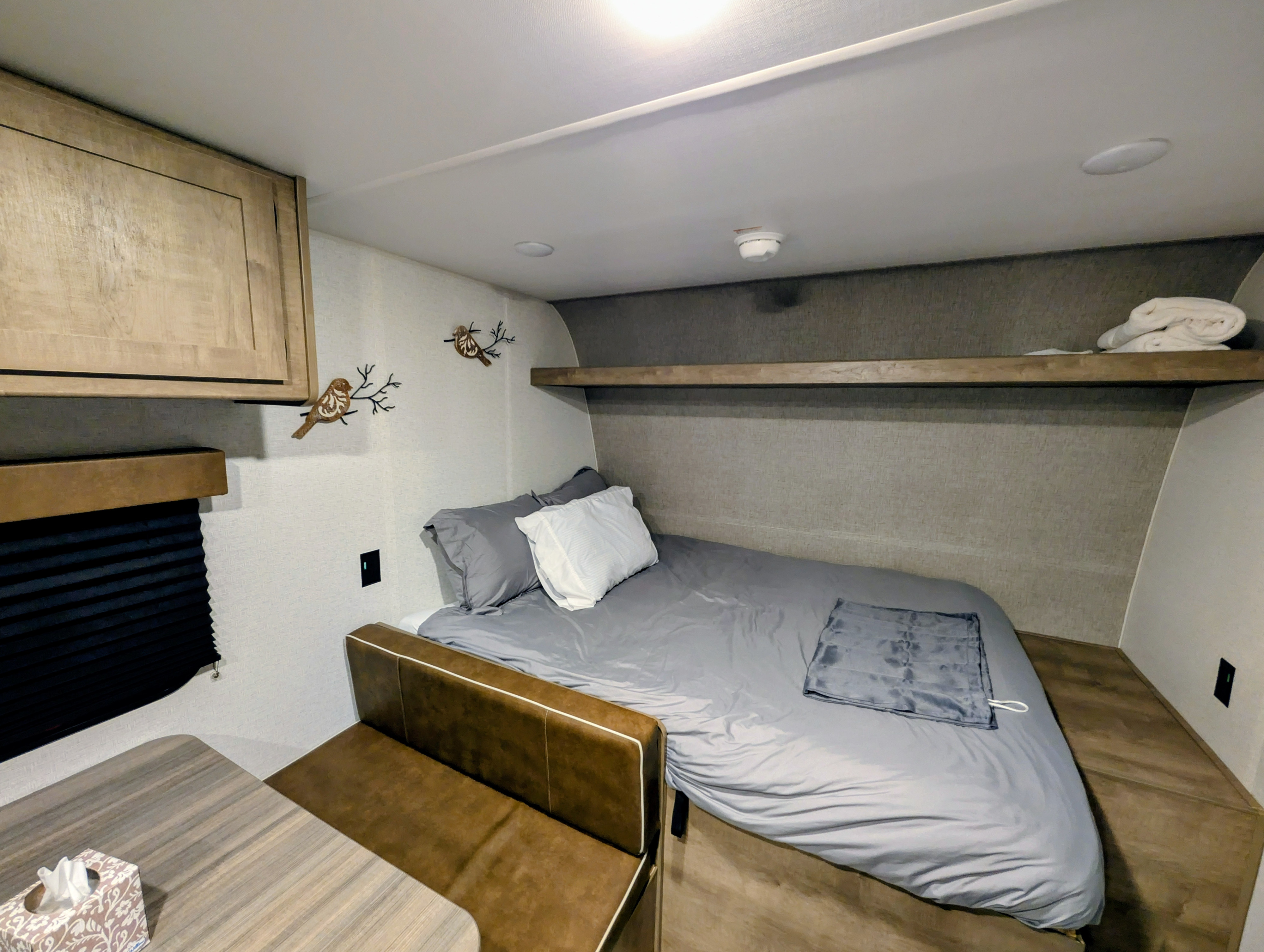 Cozy RV rental interior: A modern bedroom with a gray-linened bed, wooden shelf, and bird decor, plus a compact dining area.. Keystone RV Springdale Mini 2025