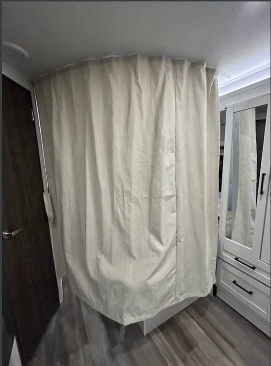 RV rental interior with light privacy curtain drawn around a private space, dark door, and white mirrored closet.. Jayco Redhawk 2026