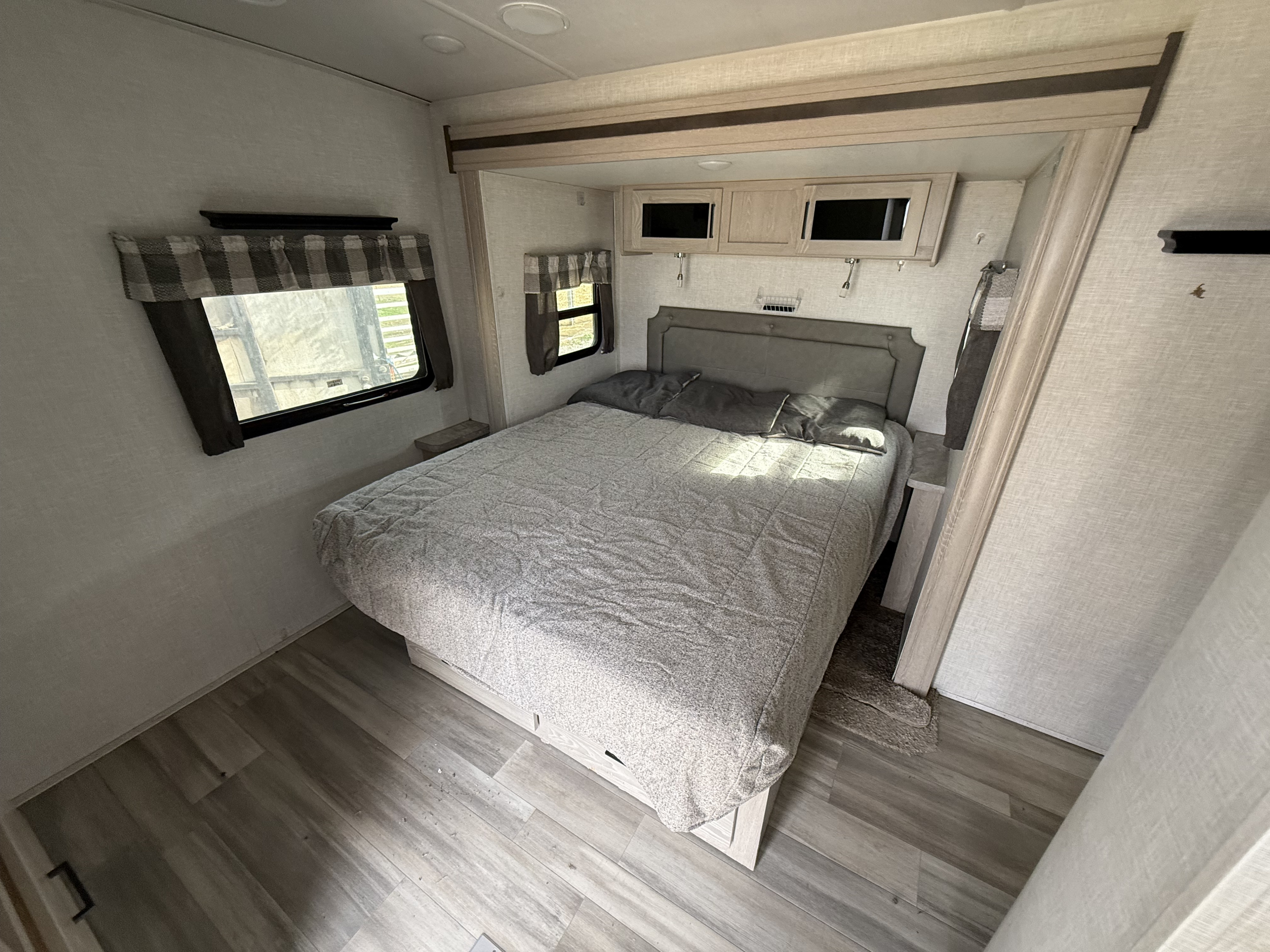 Bright RV rental bedroom with a gray bed, windows, overhead cabinets, and wood-look flooring, ideal for travel.. Forest River Flagstaff Super Lite 2021
