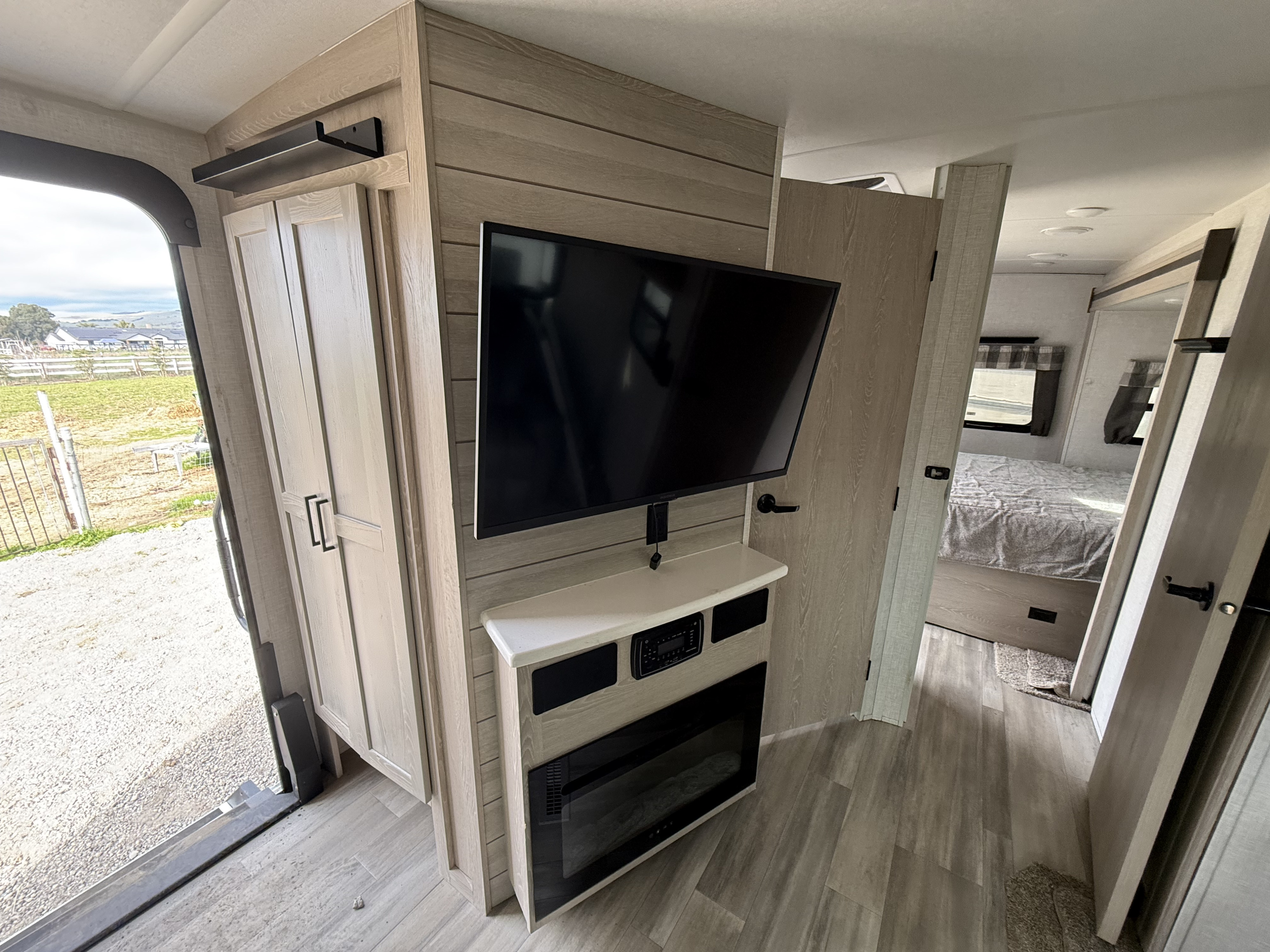 Modern rv rental interior: living area with TV, electric fireplace, wardrobe, and views into the bedroom and outdoors.. Forest River Flagstaff Super Lite 2021