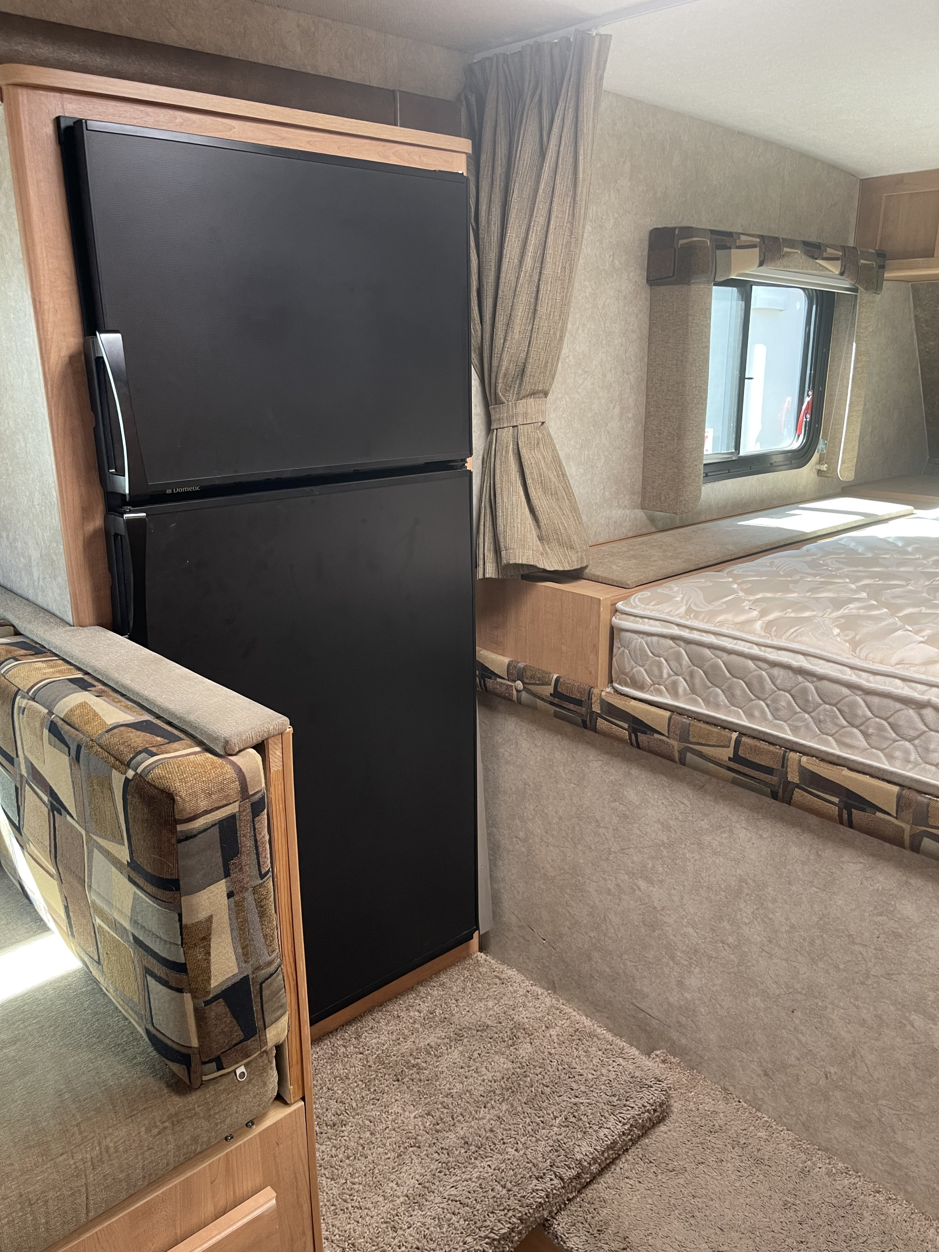 This RV rental interior showcases a Dometic refrigerator, a comfortable dinette, and a cozy bed area next to a curtained window.. Adventurer Lp Adventurer 2016