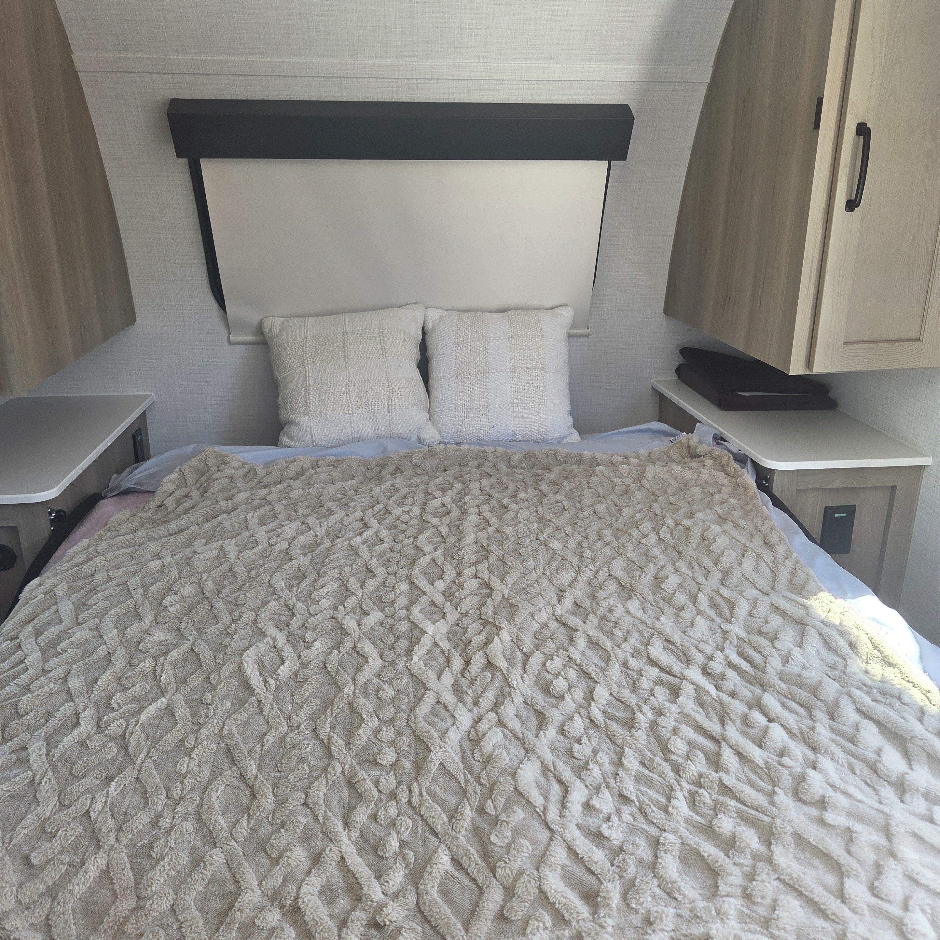 An RV rental bedroom with a comfortable bed, a textured beige blanket, two decorative pillows, and light wood cabinetry.. Forest River Rockwood Geo Pro 2024