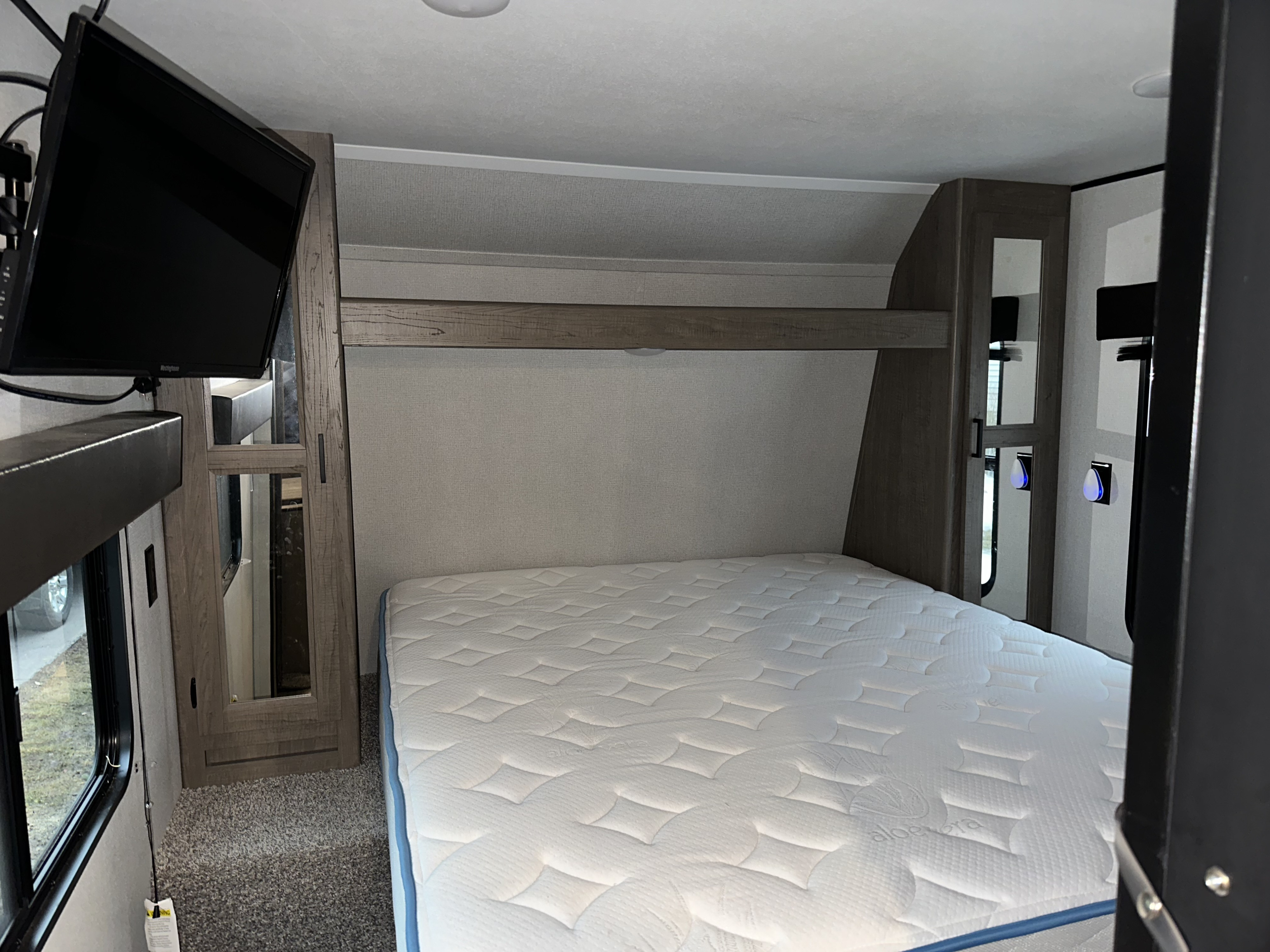 RV rental bedroom featuring a comfortable bed with a white mattress, wall-mounted TV, and storage cabinets.. Keystone RV Hideout Luxury 2021