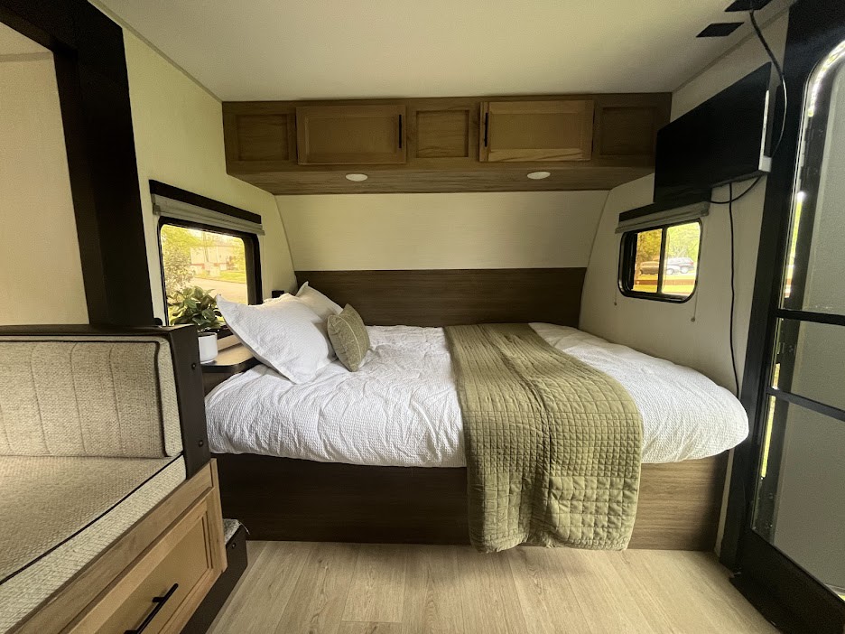 This RV rental offers a comfortable bedroom with a large bed, white & green bedding, windows, and wood-tone storage.. Forest River Cherokee Wolf Pup 2025