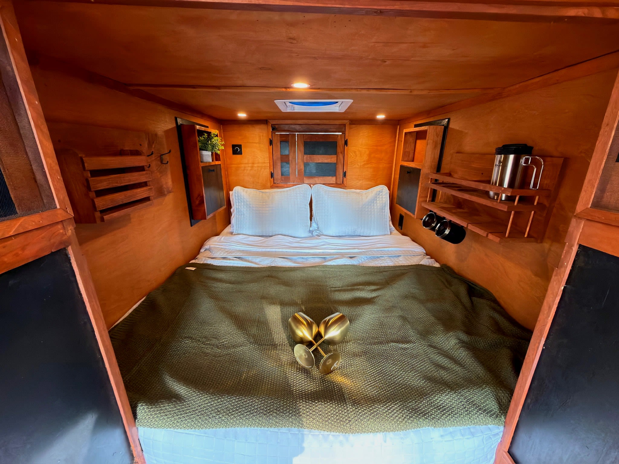 This glamping RV rental offers a cozy wood-paneled bedroom with a bed, golden glasses, and practical built-in storage.. custom CHANG 2011