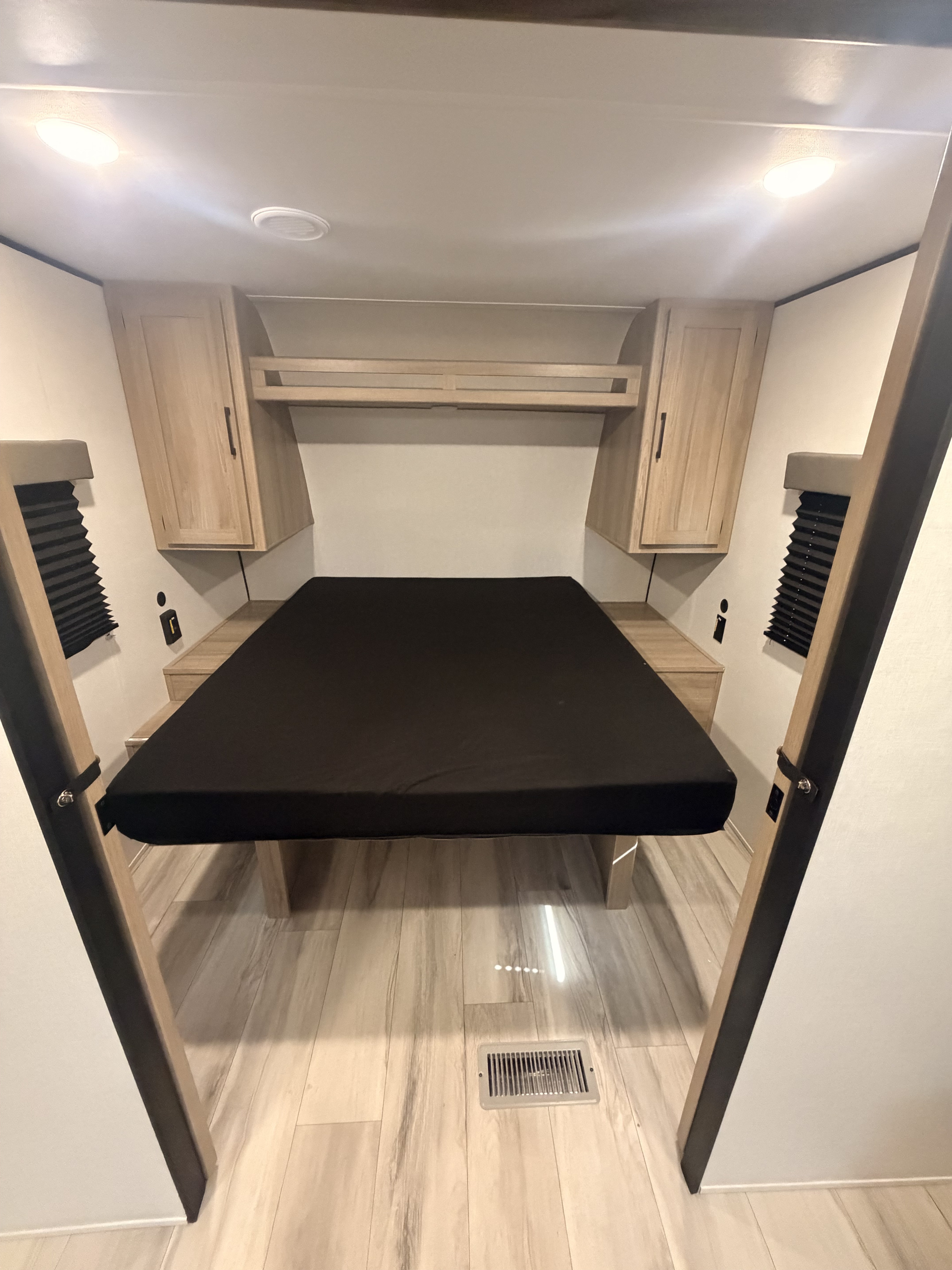 Inside an RV rental: a compact bedroom with a black mattress, light wood cabinets, and bright overhead lights.. Keystone Coleman 2026