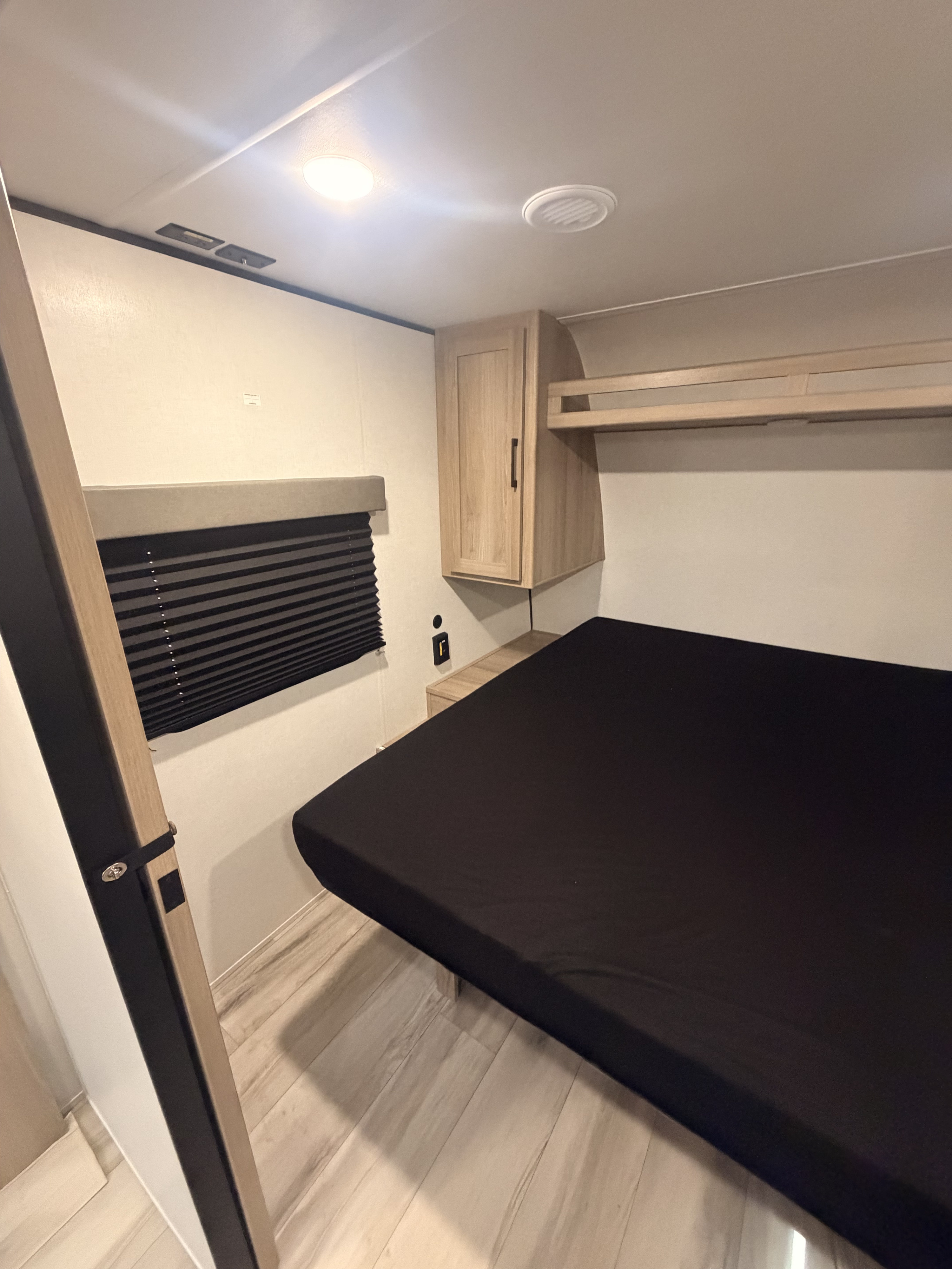 Modern RV rental bedroom with a compact bed, overhead storage, and window blind, perfect for travel.. Keystone Coleman 2026
