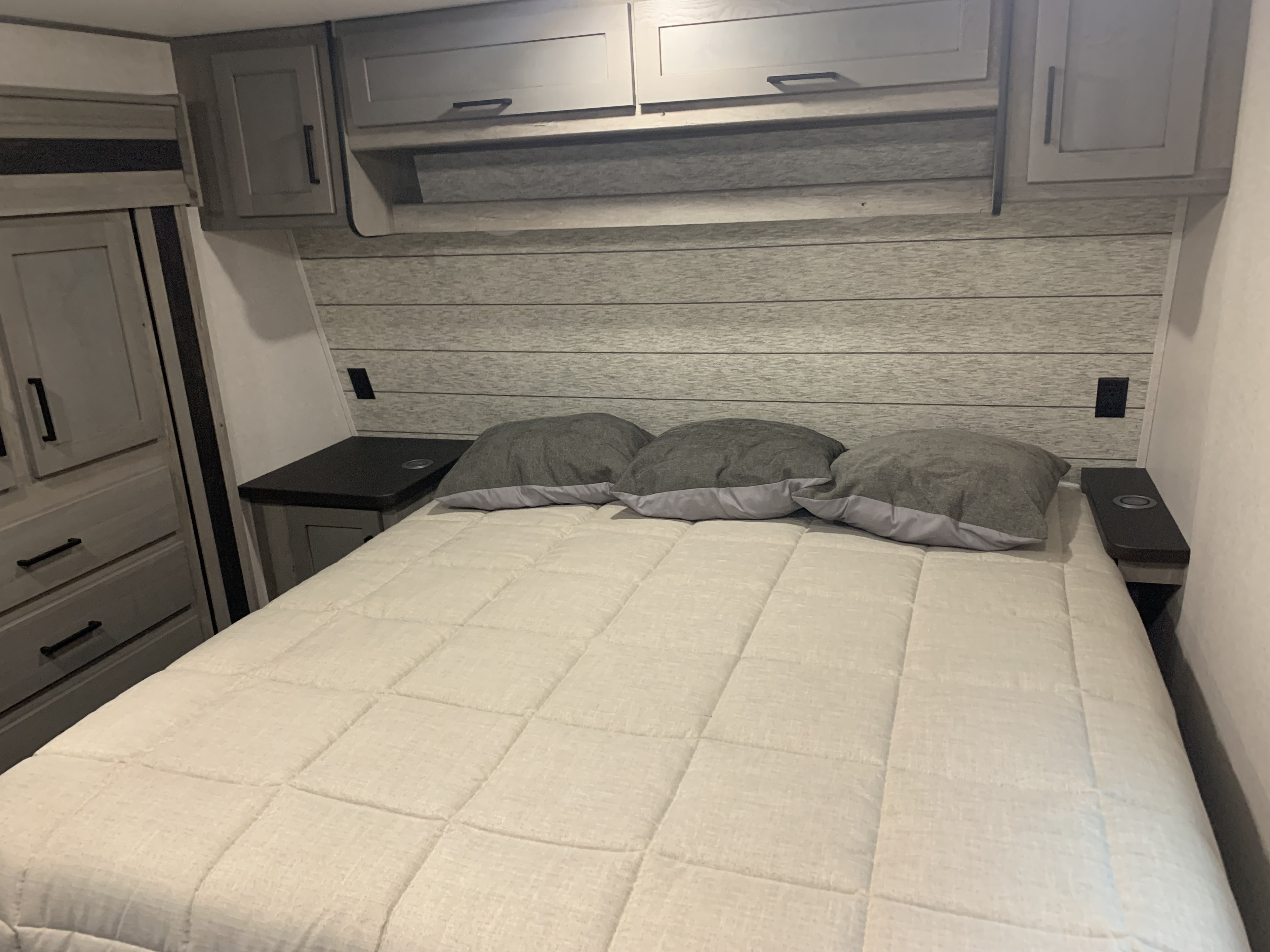 Experience comfort in this modern RV rental bedroom, featuring a cozy bed, overhead storage, and integrated nightstands.. Keystone RV Raptor Toy Hauler 2021