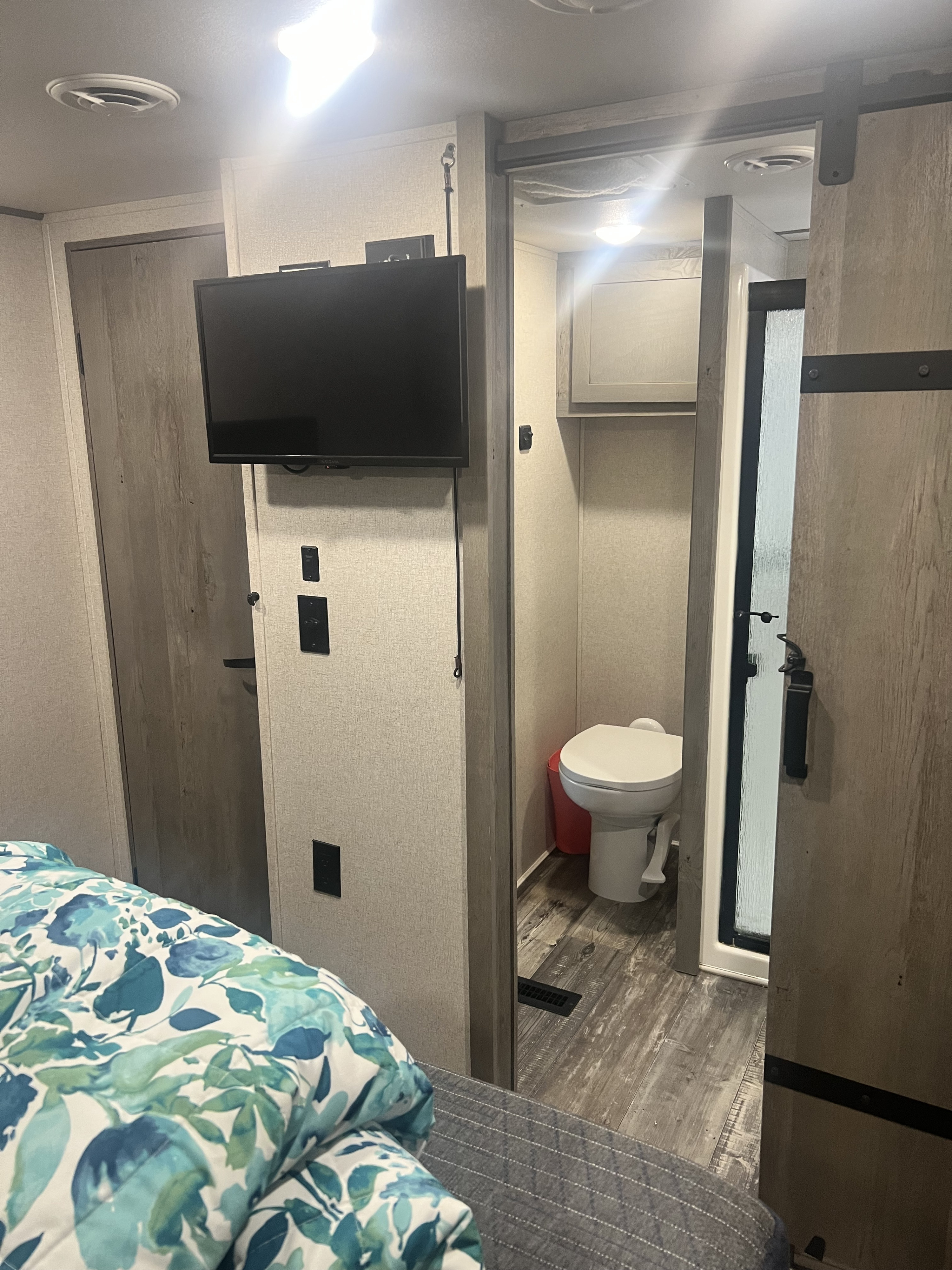 This RV rental bedroom features a TV mounted on the wall, and a sliding barn door leading to a compact bathroom with a toilet and shower.. Keystone RV Raptor Toy Hauler 2021