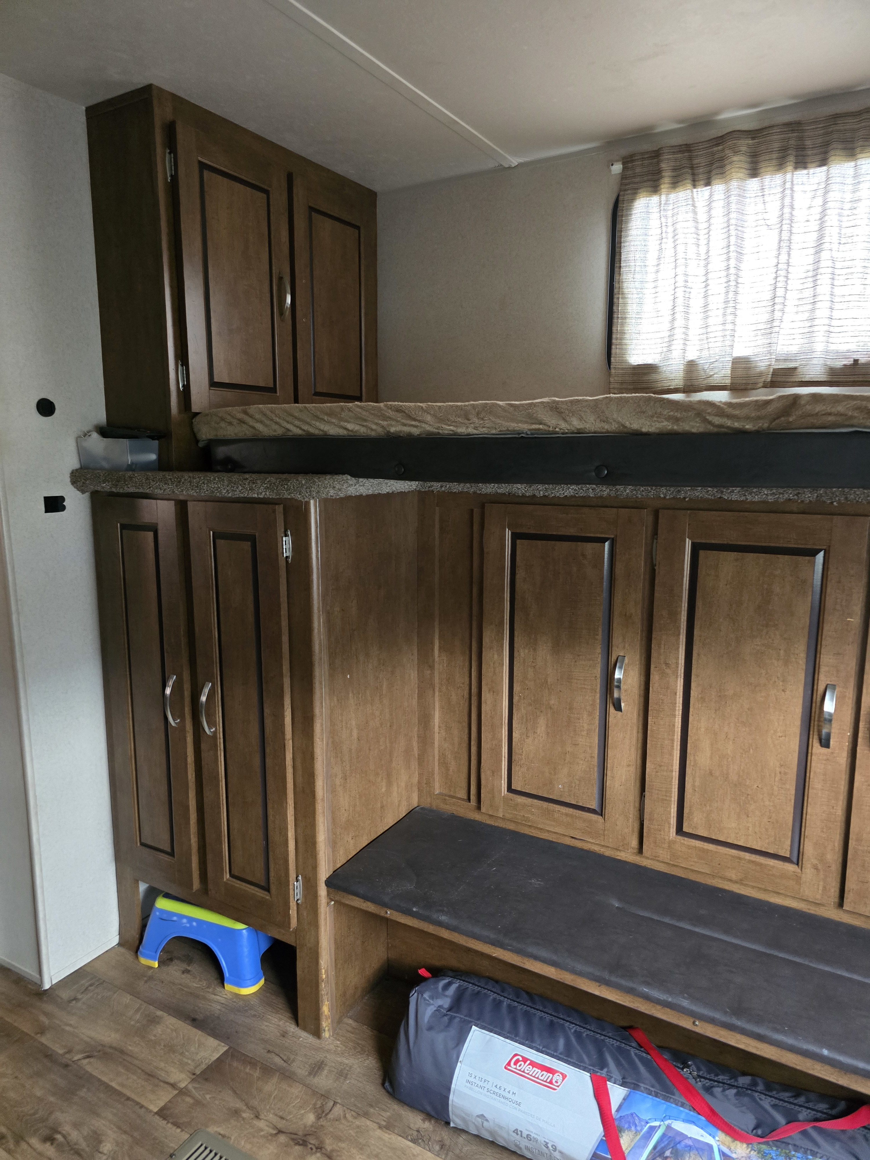 RV rental interior featuring bunk beds and storage area with wooden cabinets, a blue step stool, and a Coleman tent bag on the floor.. Forest River Salem 2017