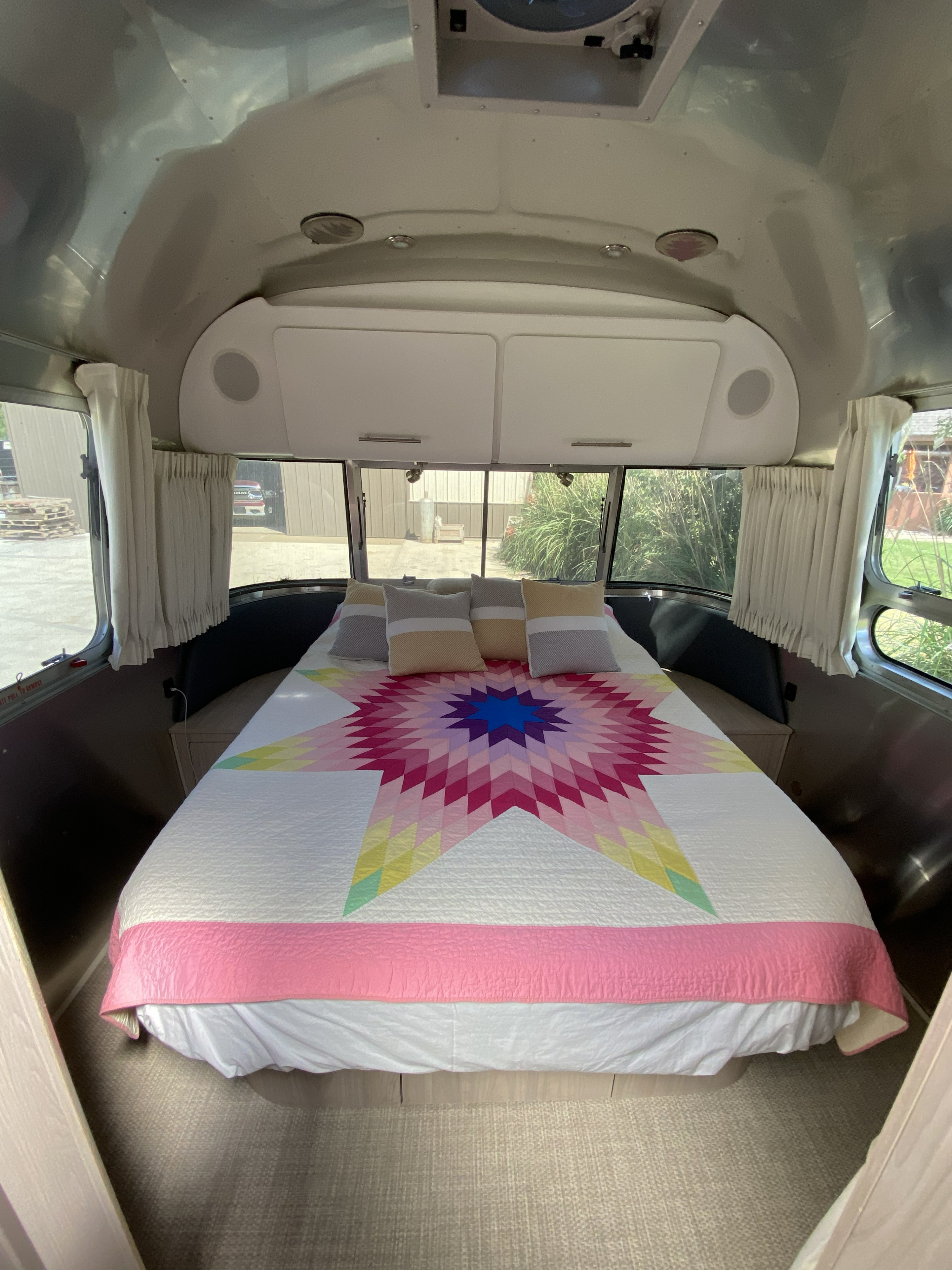 Experience comfort in this Airstream RV rental bedroom with a vibrant star quilt, overhead storage, and scenic windows.. Airstream Globetrotter 2018