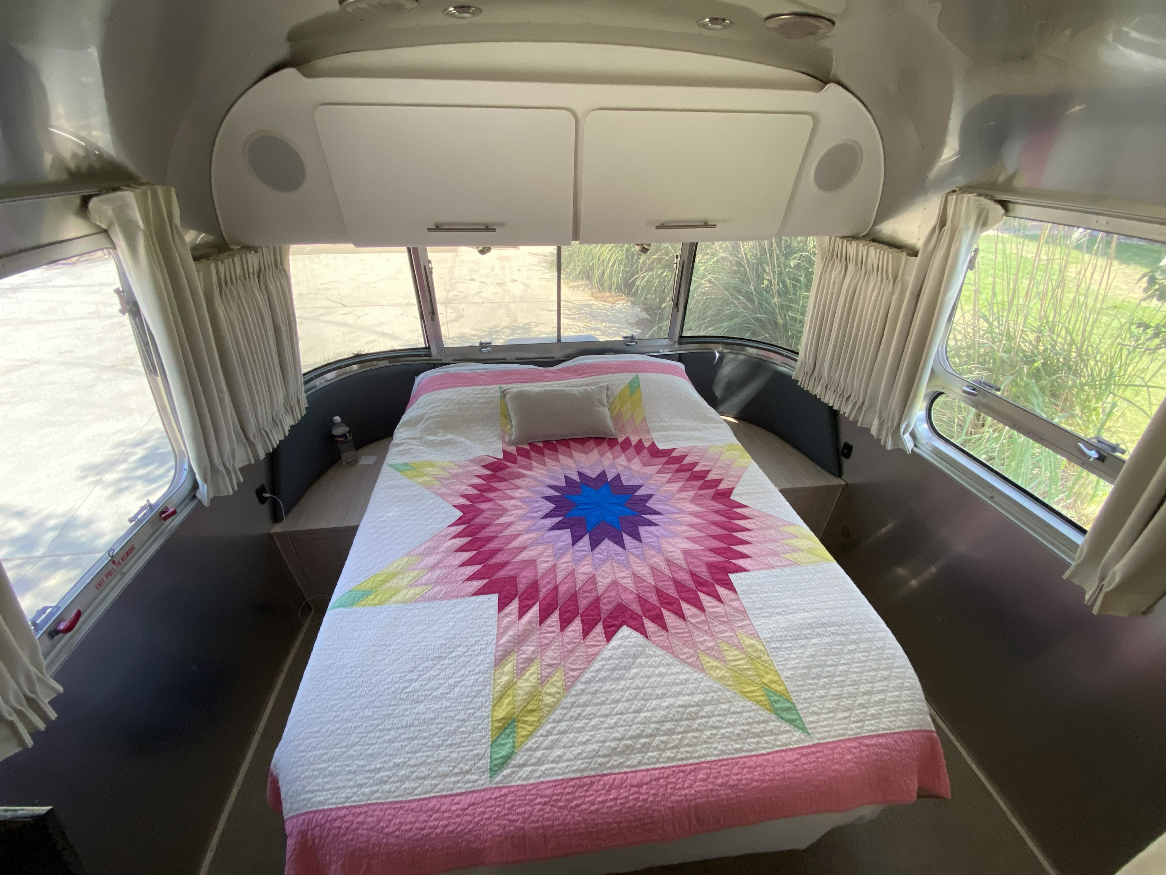 Cozy RV rental Airstream bedroom with a vibrant star quilt, large windows offering outdoor views, and convenient overhead storage.. Airstream Globetrotter 2018