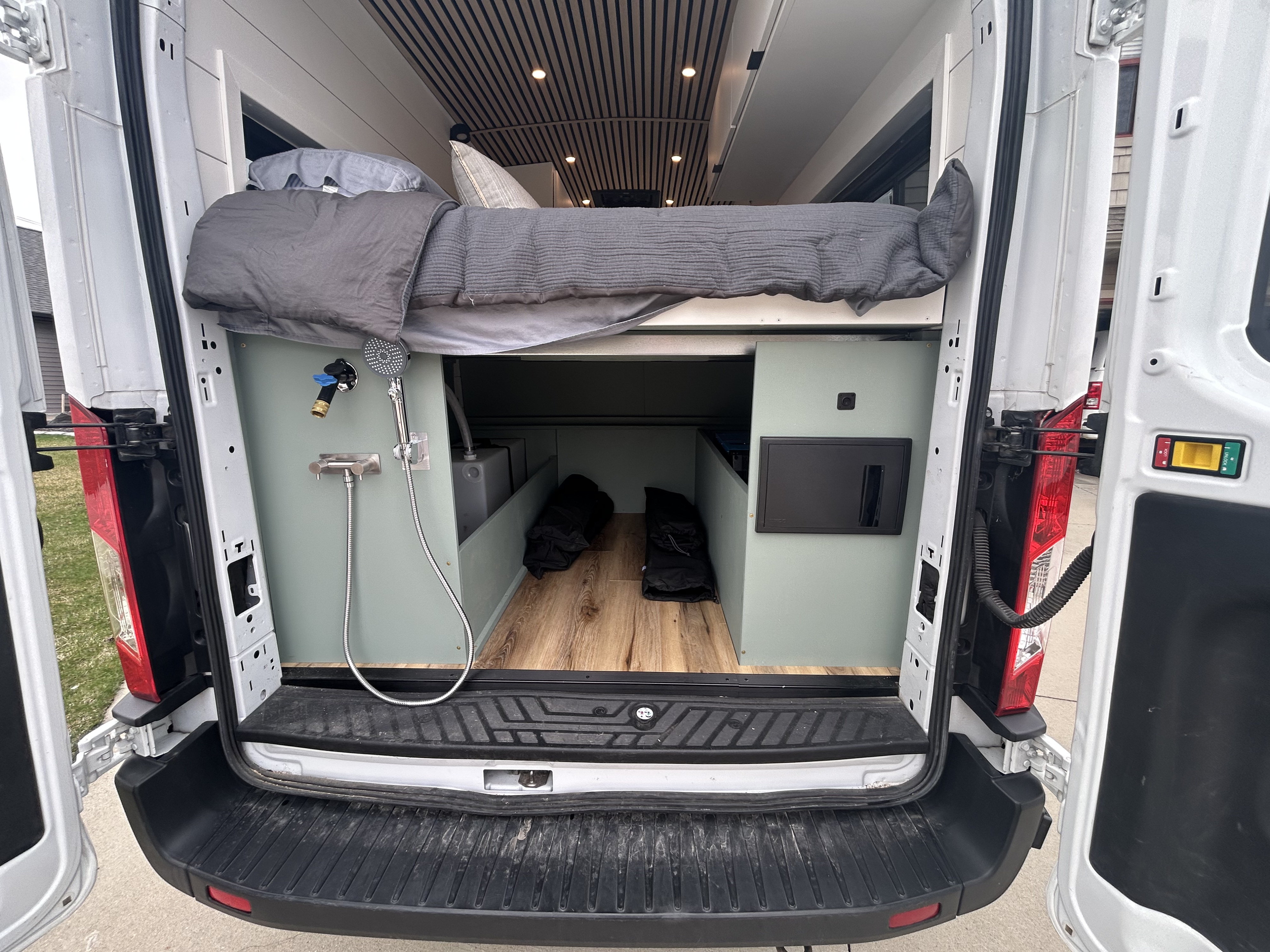 RV rental camper van interior: rear view with raised bed, outdoor shower, under-bed storage, and electrical panel.. Ford Transit 250 2020