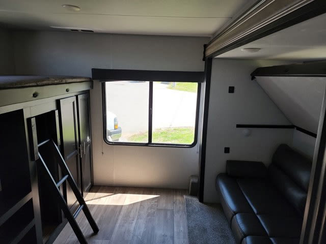 RV rental interior: Modern living space featuring bunk beds with a ladder, a bright window, and a dark sofa.. Forest River Cherokee 2022