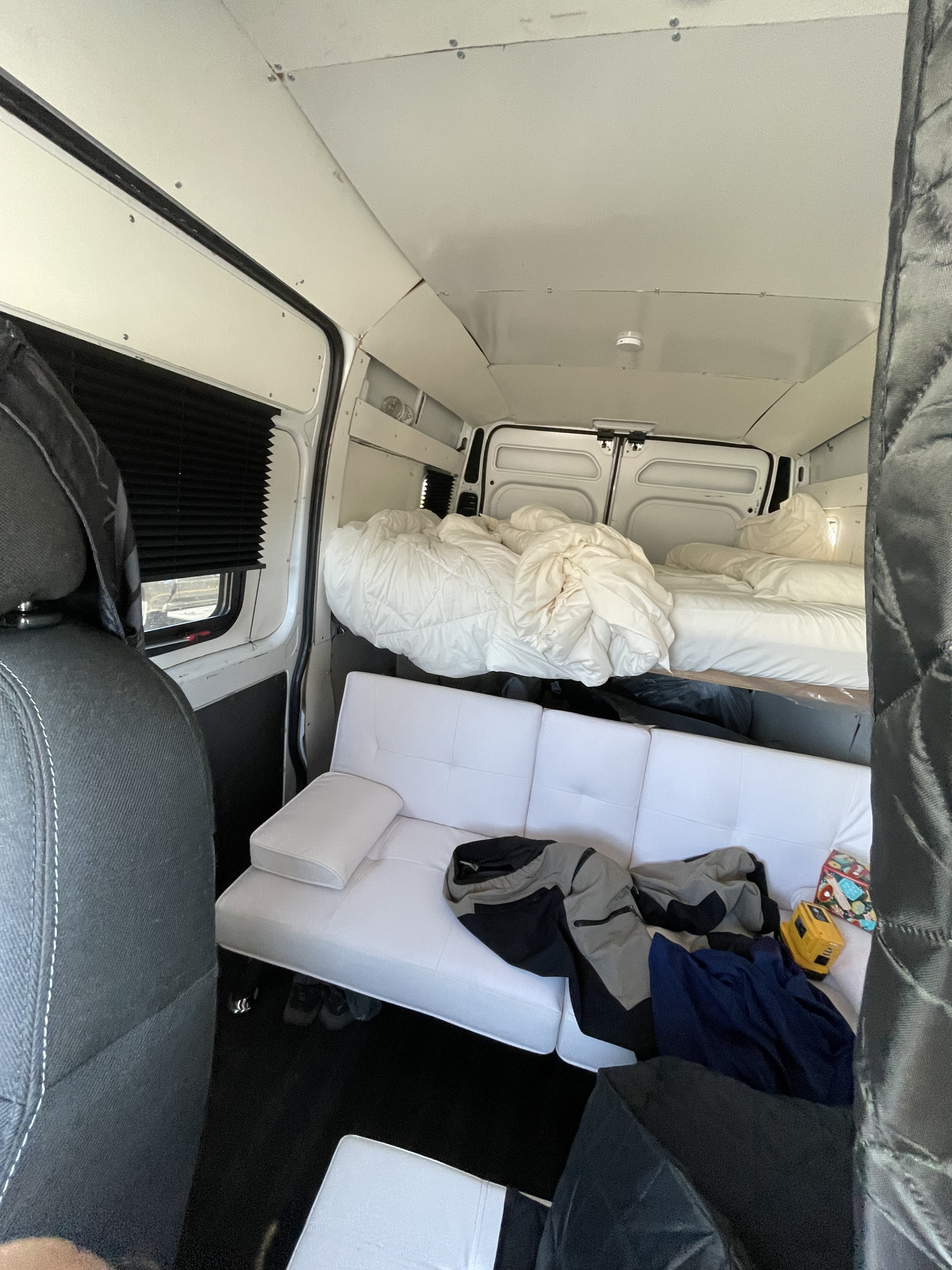 Inside an RV rental camper van with a cozy bed, white sofa, and window blinds. Ready for adventure!. Ram Pro Master 1500 2020