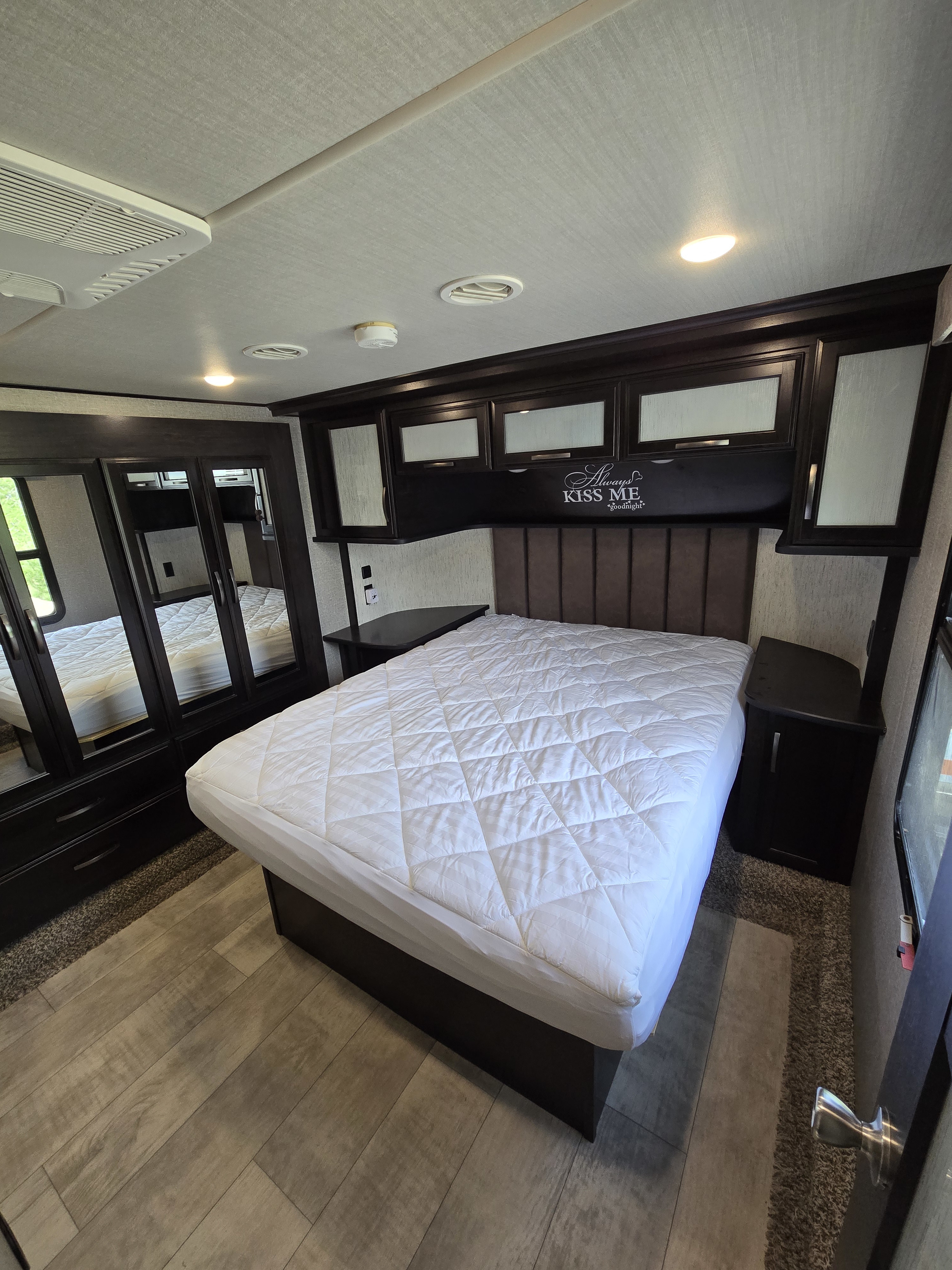 Cozy RV rental bedroom with a plush bed, mirrored wardrobe, and overhead storage, ideal for comfortable travel.. Grand Design Momentum 2019