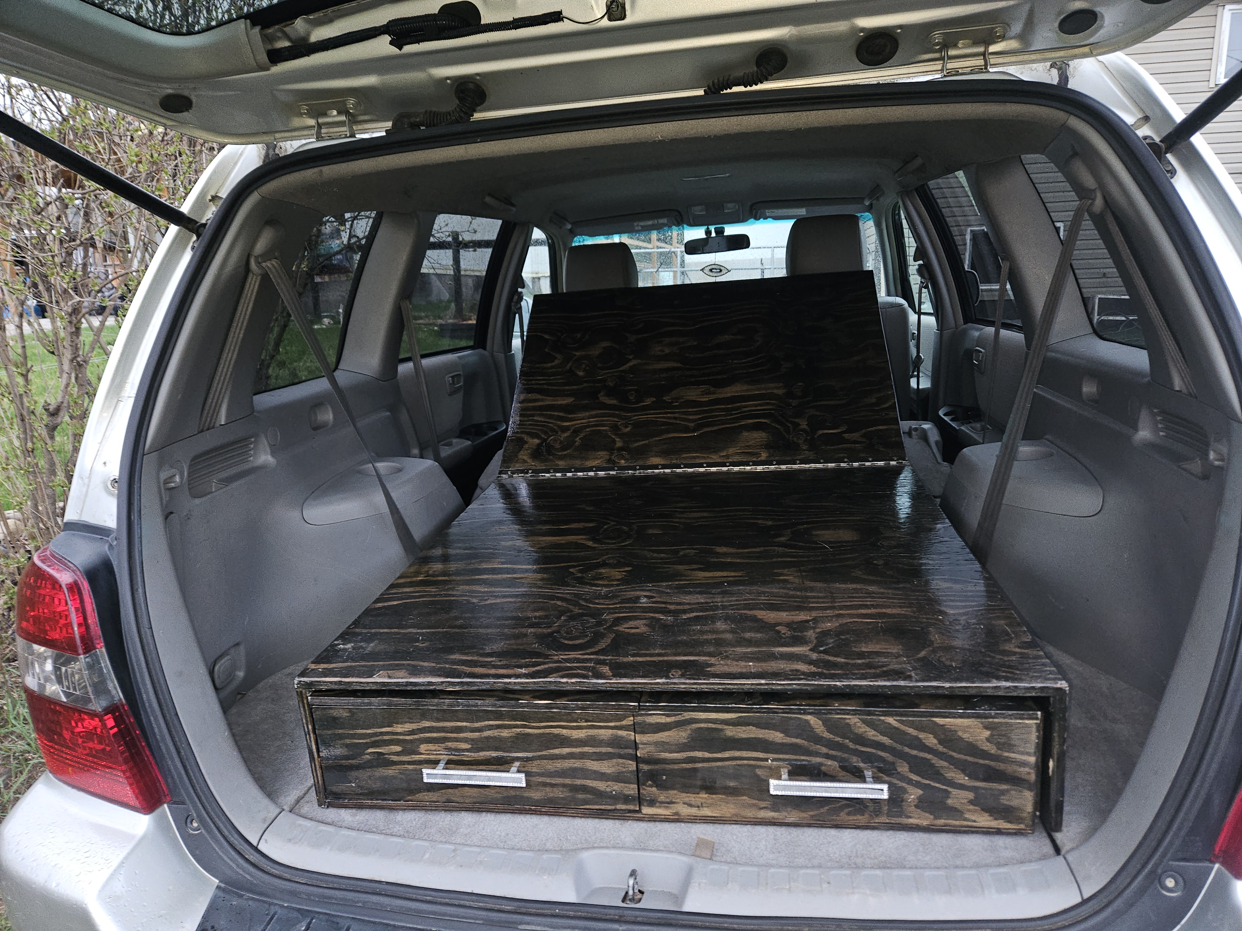 Silver SUV's trunk features a dark wood sleeping platform with storage drawers, ready for car camping or an RV rental trip.. Toyota Highlander 2004