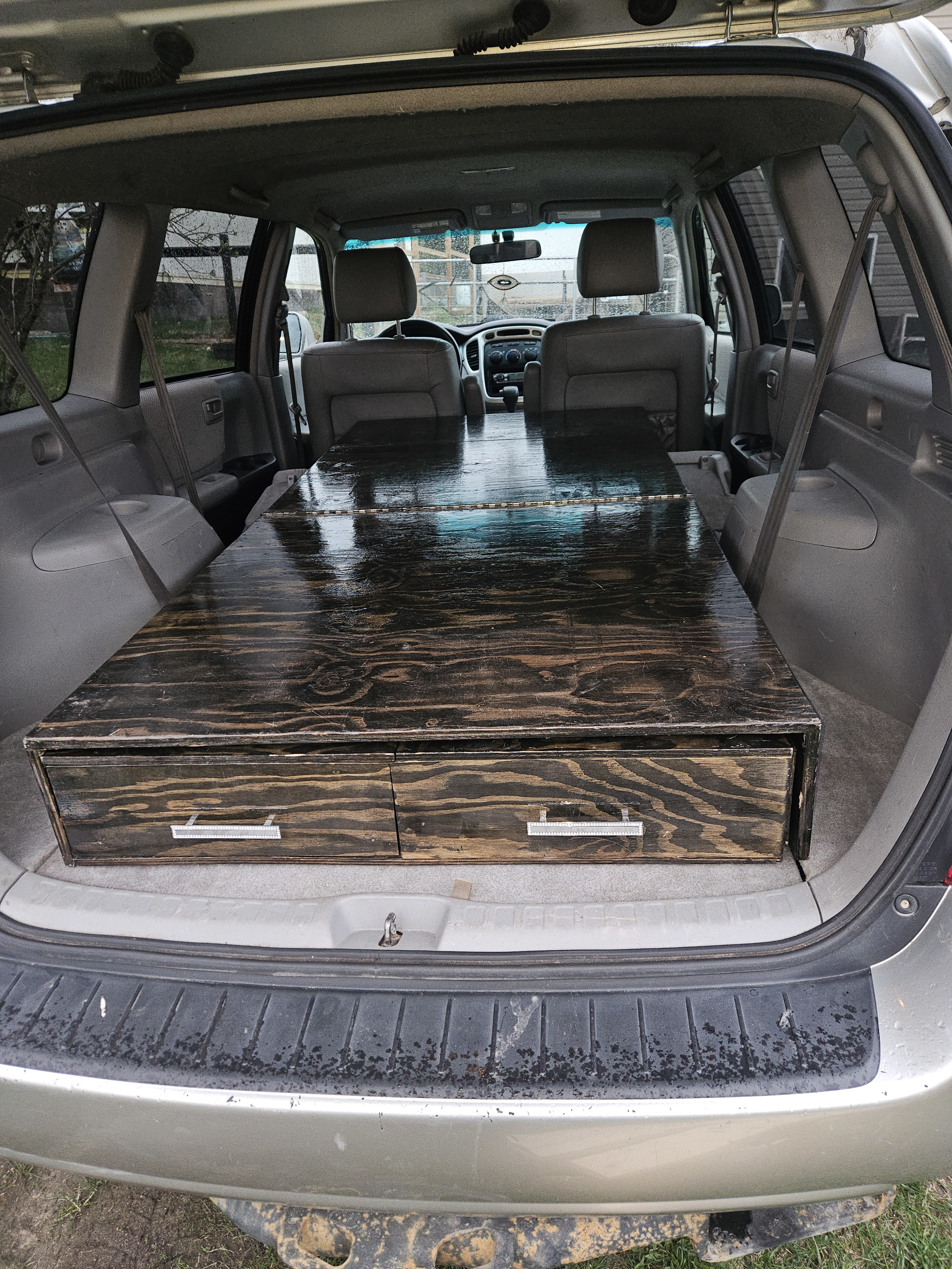 DIY car camping conversion: a custom wooden sleeping platform with drawers in an SUV, perfect for an RV rental trip.. Toyota Highlander 2004