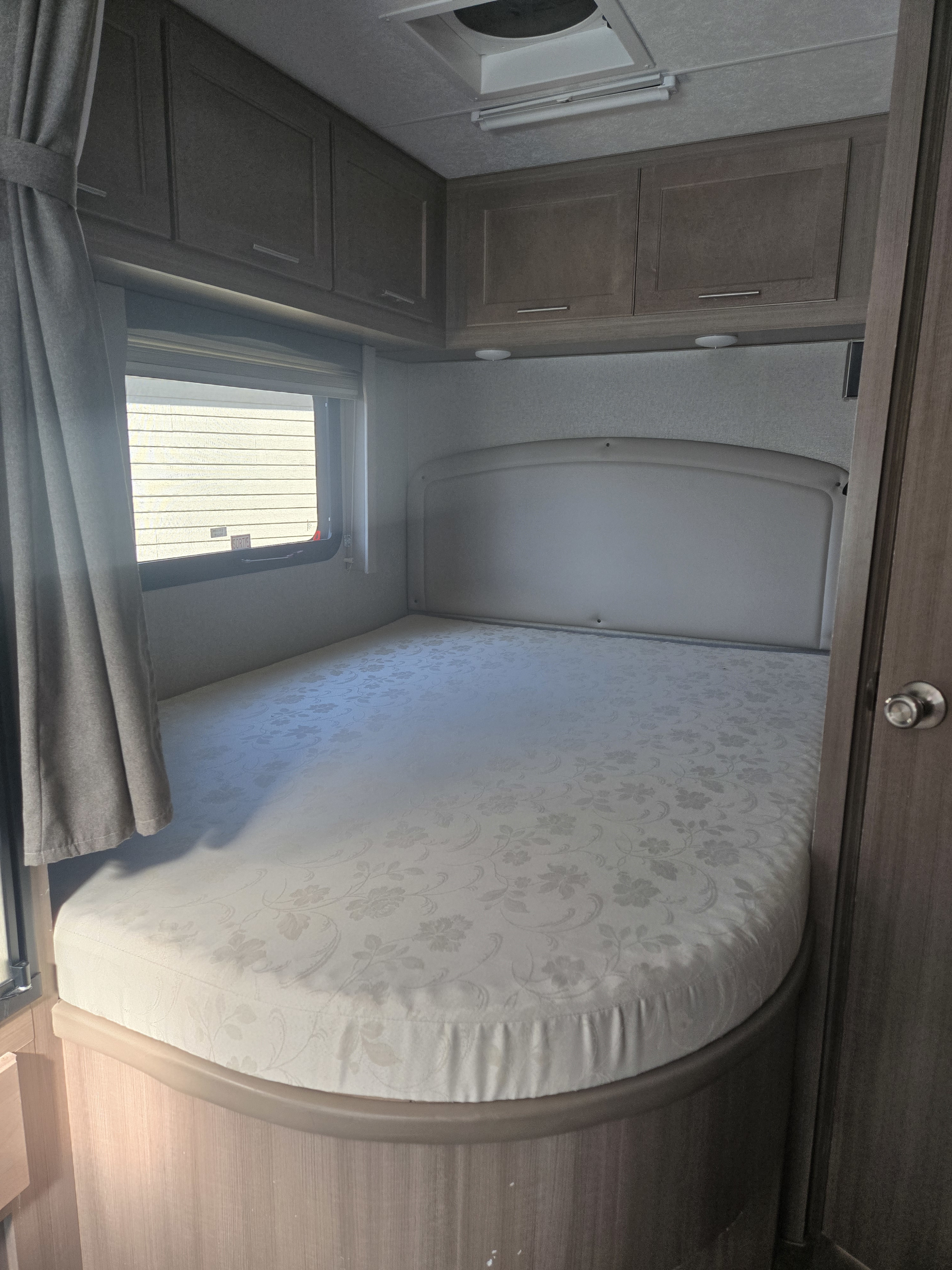 Inside an RV rental: a neat bedroom featuring a curved bed with a floral mattress, headboard, window, and storage cabinets.. ALP Adventurer 23R 2022