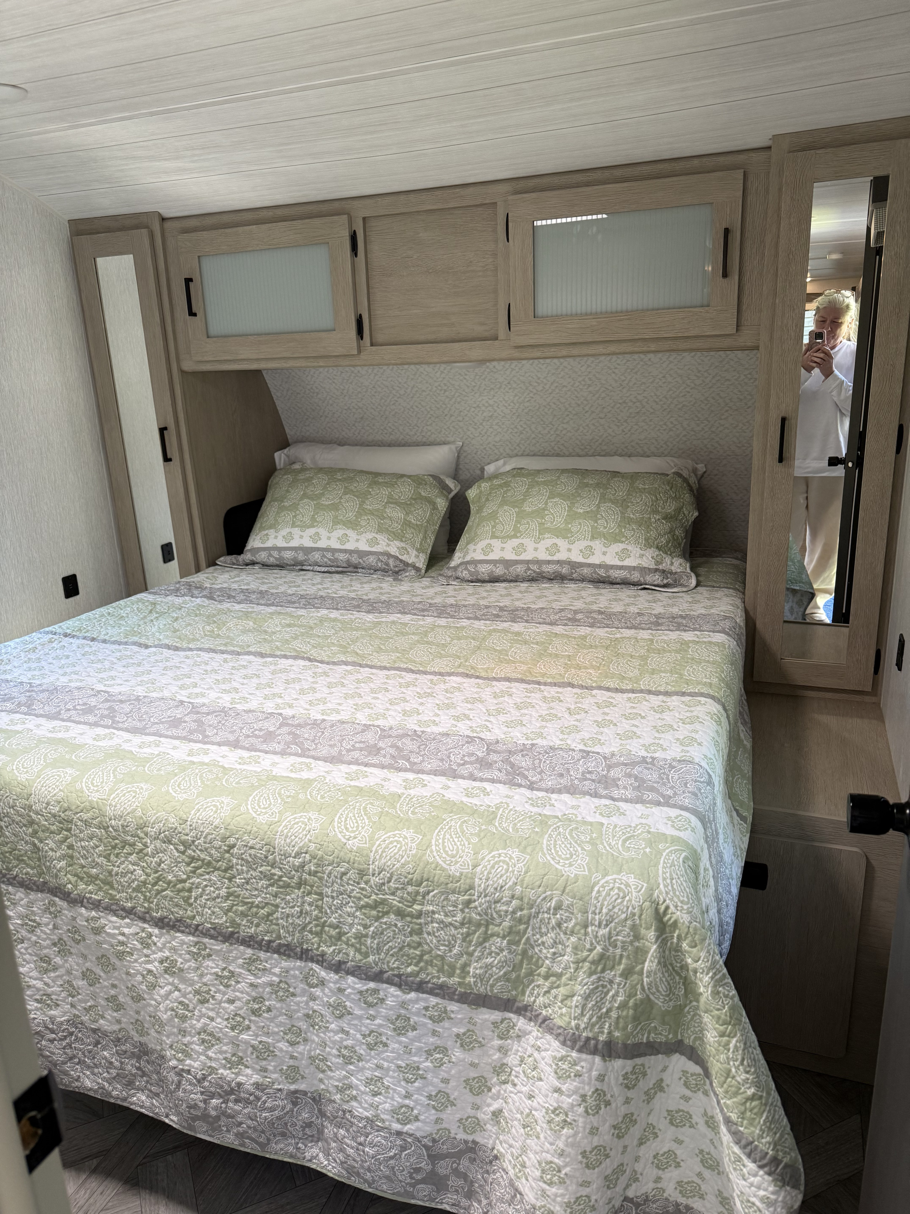 RV rental bedroom. Queen bed with green/grey paisley quilt, overhead cabinets, and mirrored closet. Bright, modern interior.. Forest River Wildwood FSX Platinum 2023