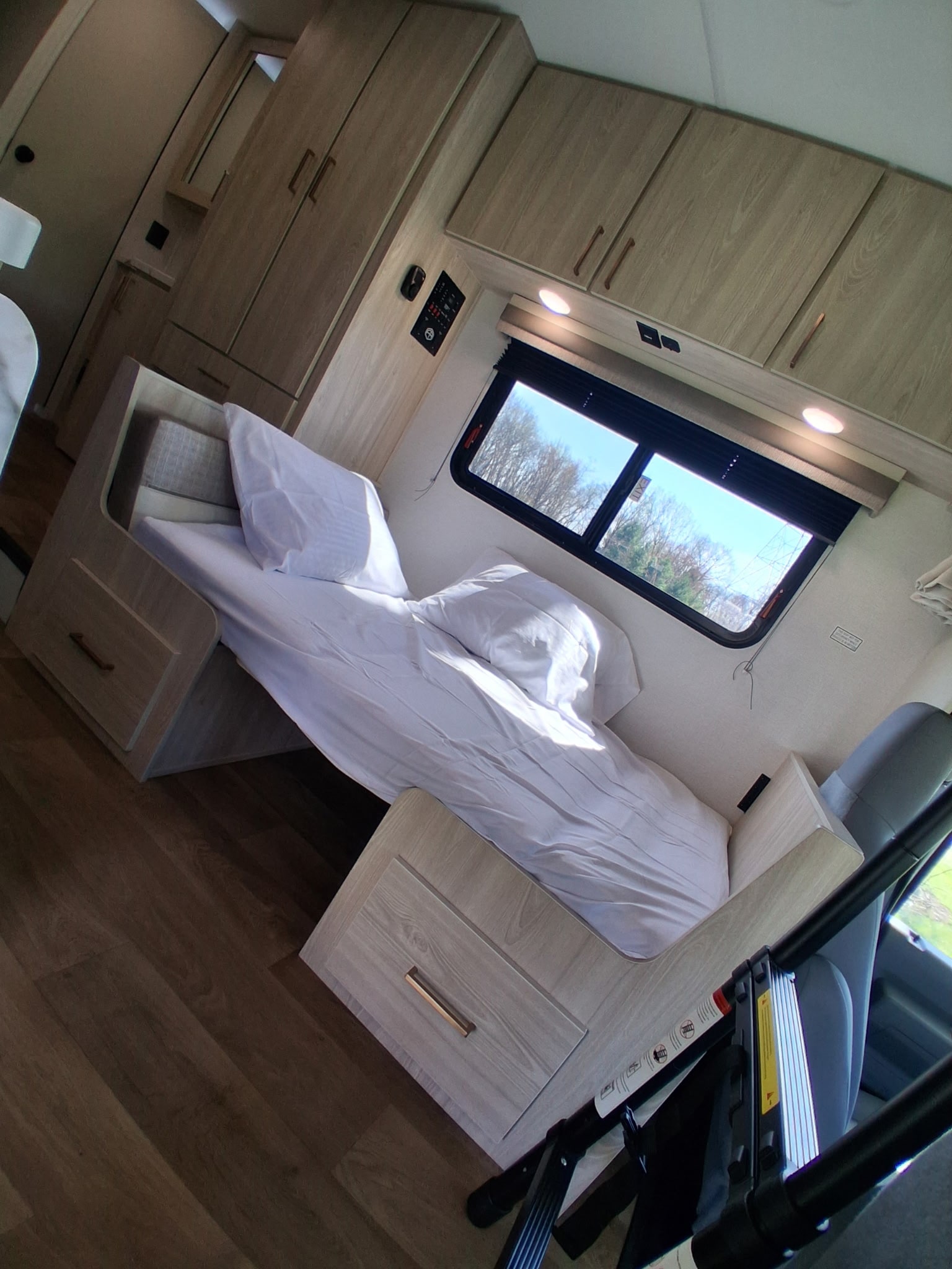 Cozy bunk bed area in an RV rental, featuring light wood cabinets, an access ladder, and a window with a scenic view.. East to West Entrada 2026