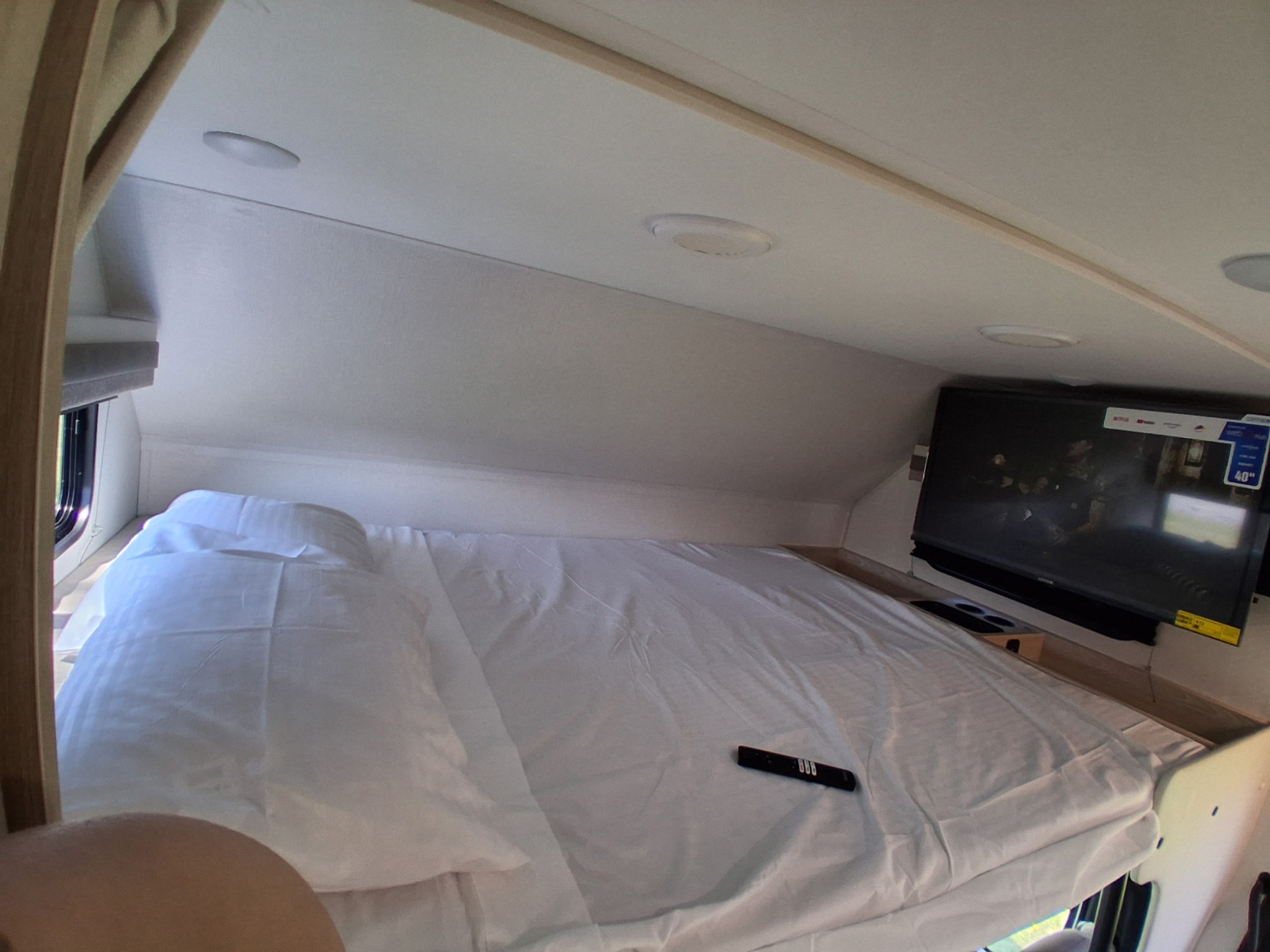 Comfortable RV rental sleeping area with TV, showing a neatly made bed and remote.. East to West Entrada 2026