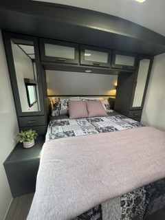 Experience comfort in this cozy RV rental bedroom. Features a bed with patterned linens, pink accents, and mirrored storage.. Keystone RV Bullet Ultra Lite 2022