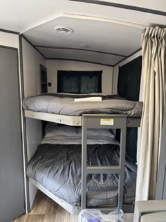 This cozy rv rental features sturdy bunk beds with dark gray bedding and a ladder, ideal for family camping. RV interior view.. Keystone RV Bullet Ultra Lite 2022