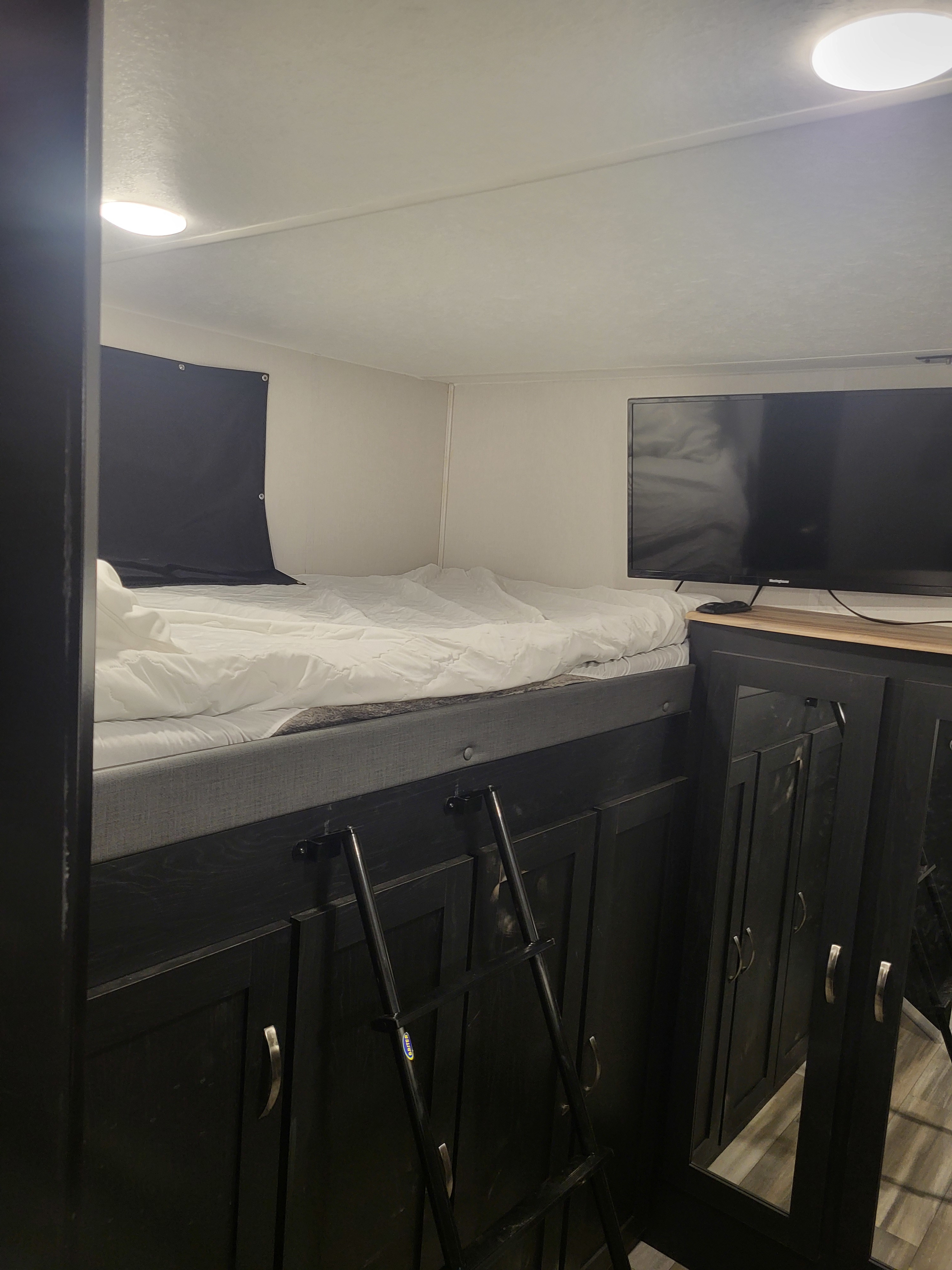 Cozy RV rental bedroom with elevated bunk bed, flat-screen TV, ladder access, and ample cabinet storage.. Coachmen Freedom Express liberty edition 326bhdsle 2023