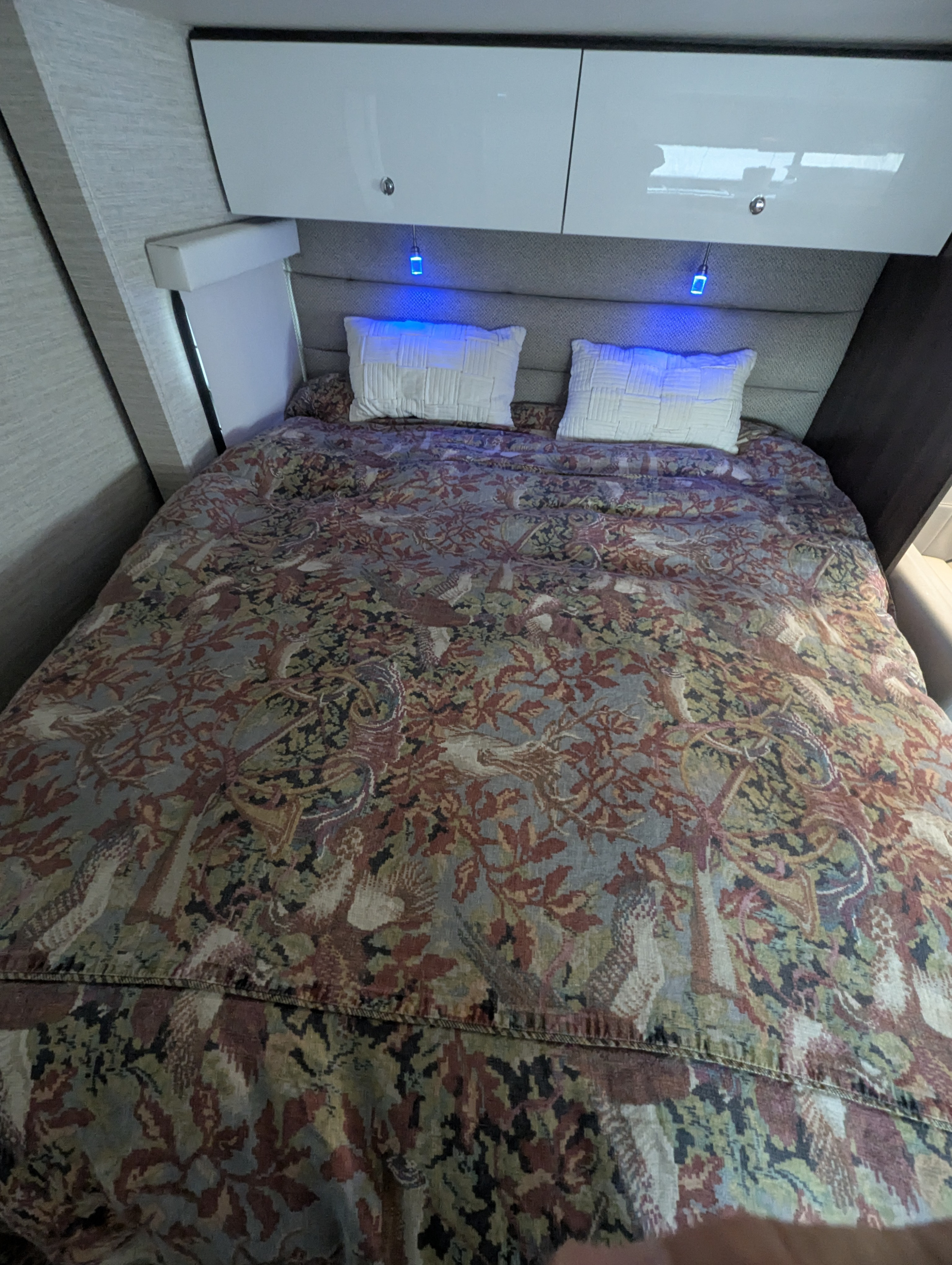 Cozy RV rental bedroom featuring a bed with a detailed patterned duvet, overhead cabinets, and blue accent lights above the headboard.. Winnebago Navion 2021