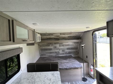 Explore this cozy RV rental interior: a bedroom with a unique wall, storage cabinets, a dinette, and an open door to the outside.. Coleman Lantern 2023