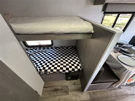 RV rental's cozy interior features bunk beds (top cream, bottom checkered), an exit window, and a dining table.. Coleman Lantern 2023