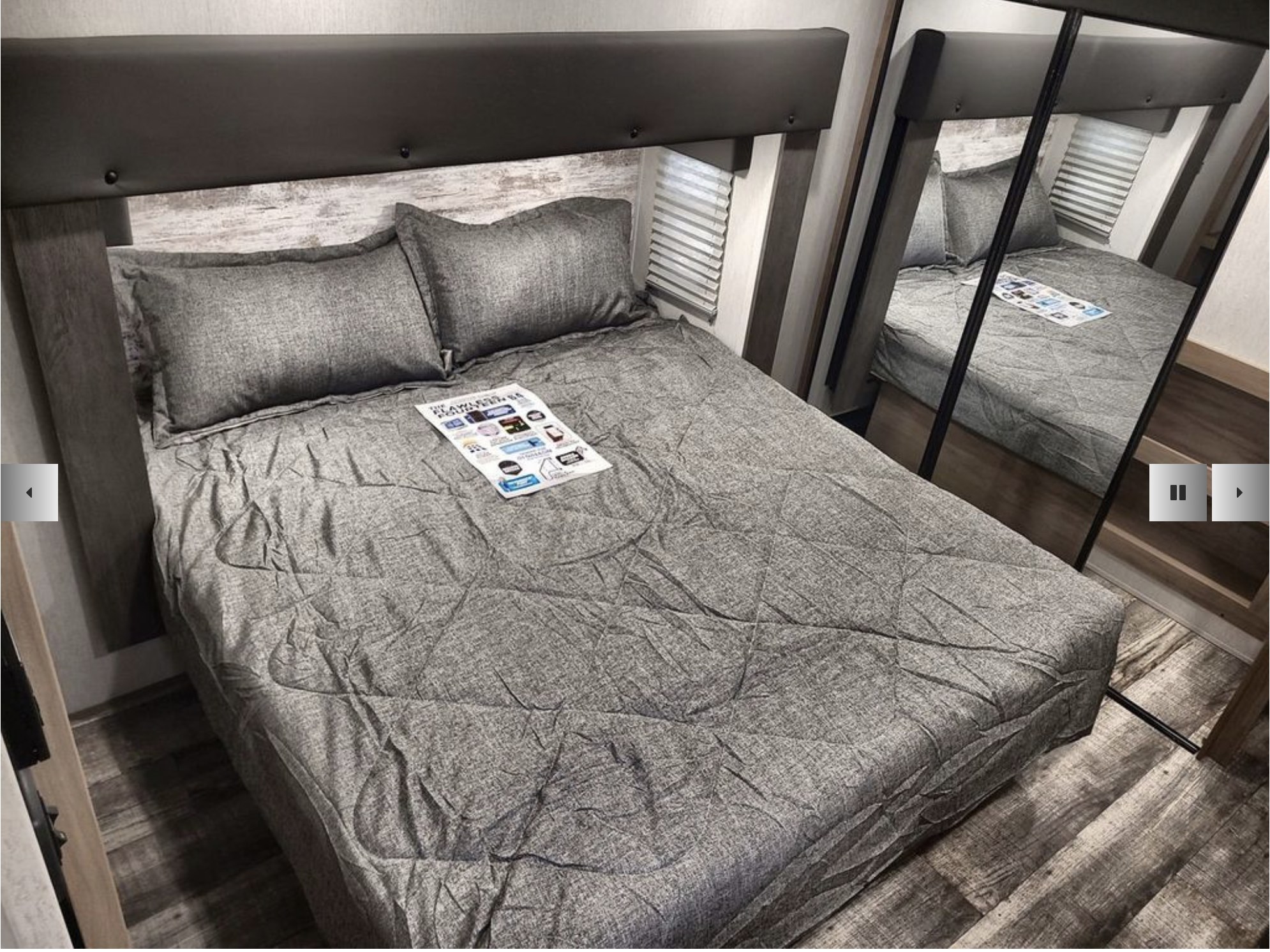 RV rental bedroom with a bed featuring gray bedding, padded headboard, wood-look floor, and mirrored closet.. Forest River Cherokee Arctic Wolf 2024