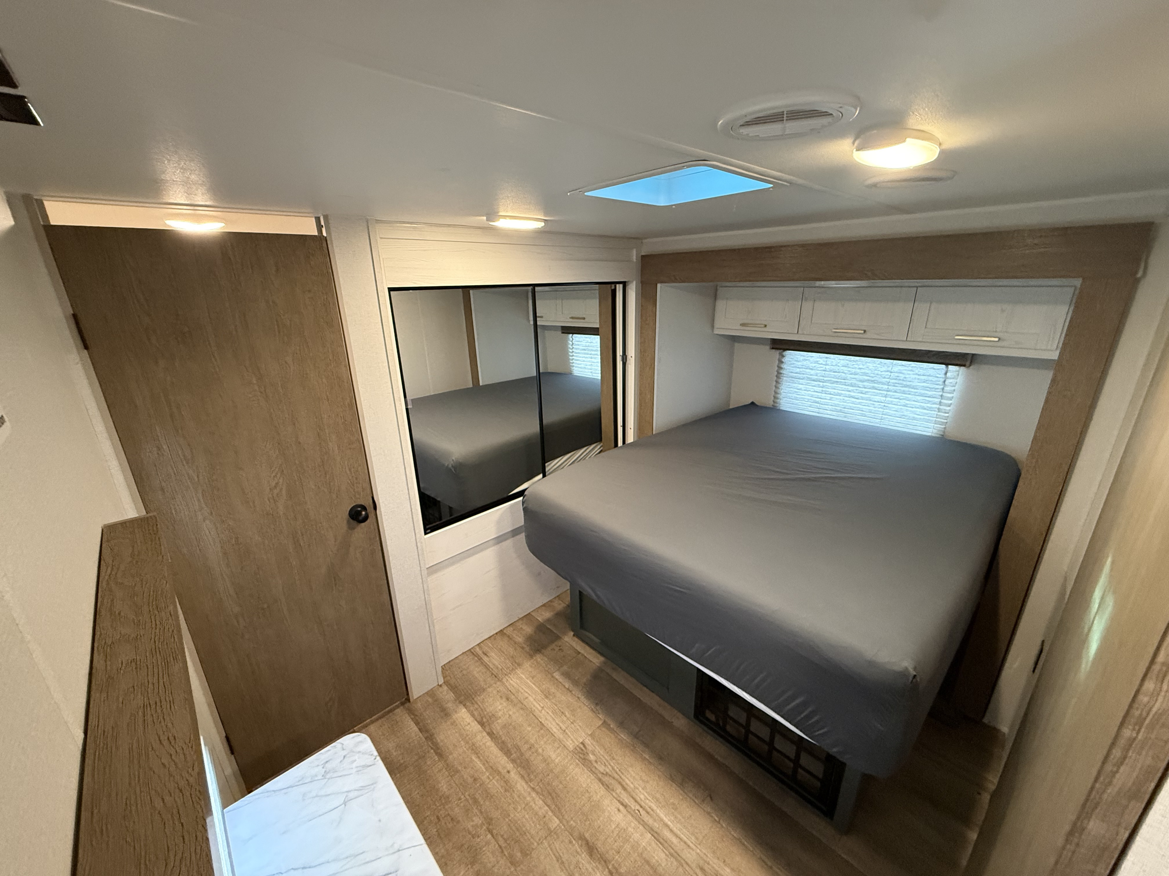 Comfortable RV rental bedroom with a gray bed, overhead cabinets, and wood flooring, perfect for your next adventure.. Heartland RVs Eddie Bauer 2025