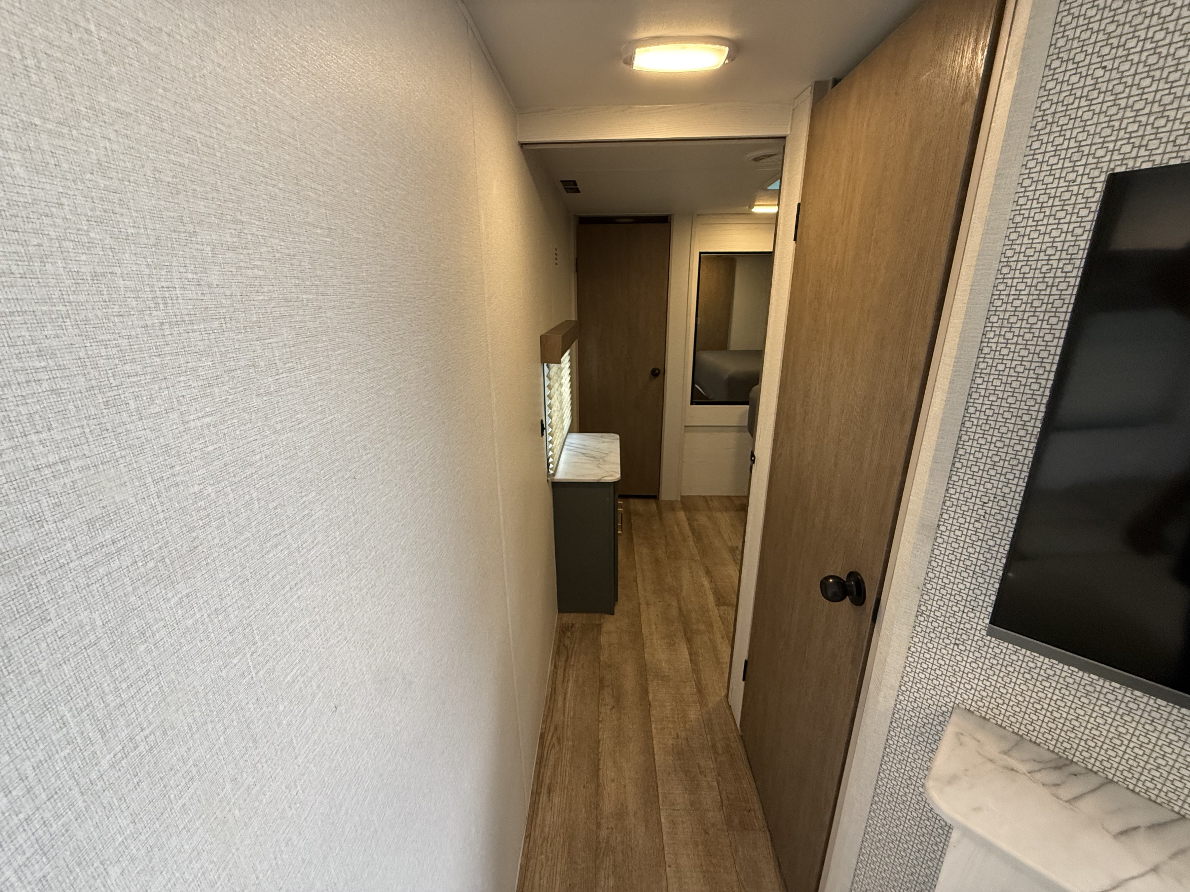 A compact rv rental hallway features light textured walls, wooden doors, and a vanity, leading to a bright bedroom.. Heartland RVs Eddie Bauer 2025