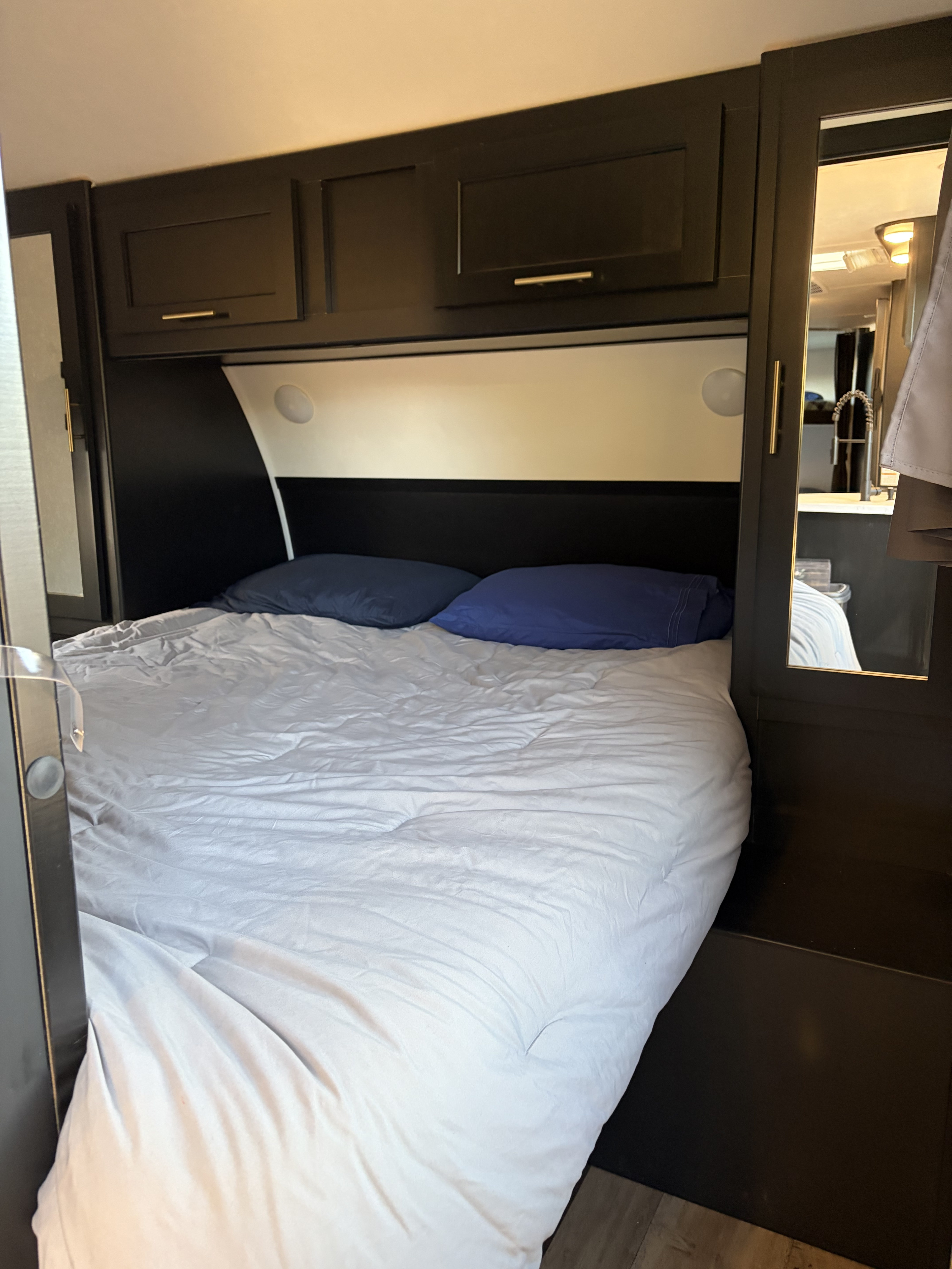Relaxing RV rental bedroom features a comfortable bed with blue pillows, dark wood cabinets, and built-in lighting.. Forest River Cherokee Grey Wolf 2022