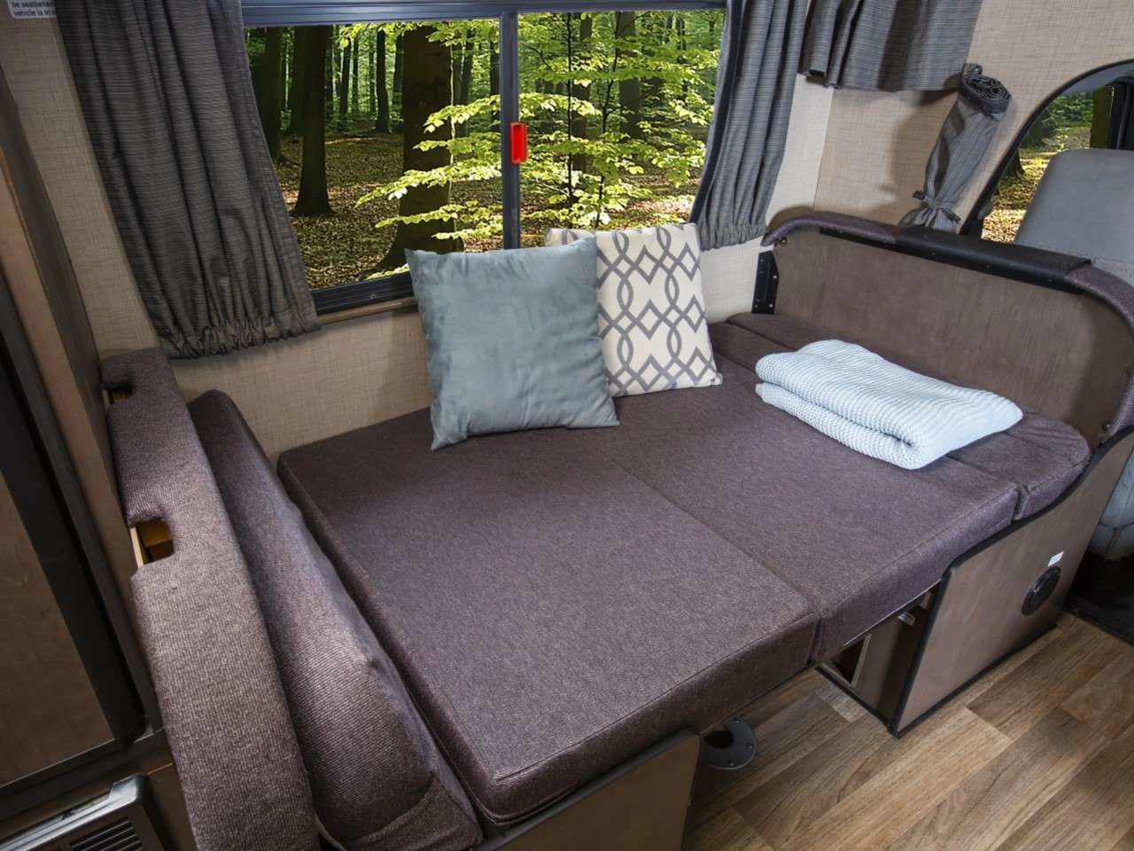 RV rental interior featuring a cozy bed/seating area with pillows and a blanket, showcasing a forest view.. Thor Majestic 2020