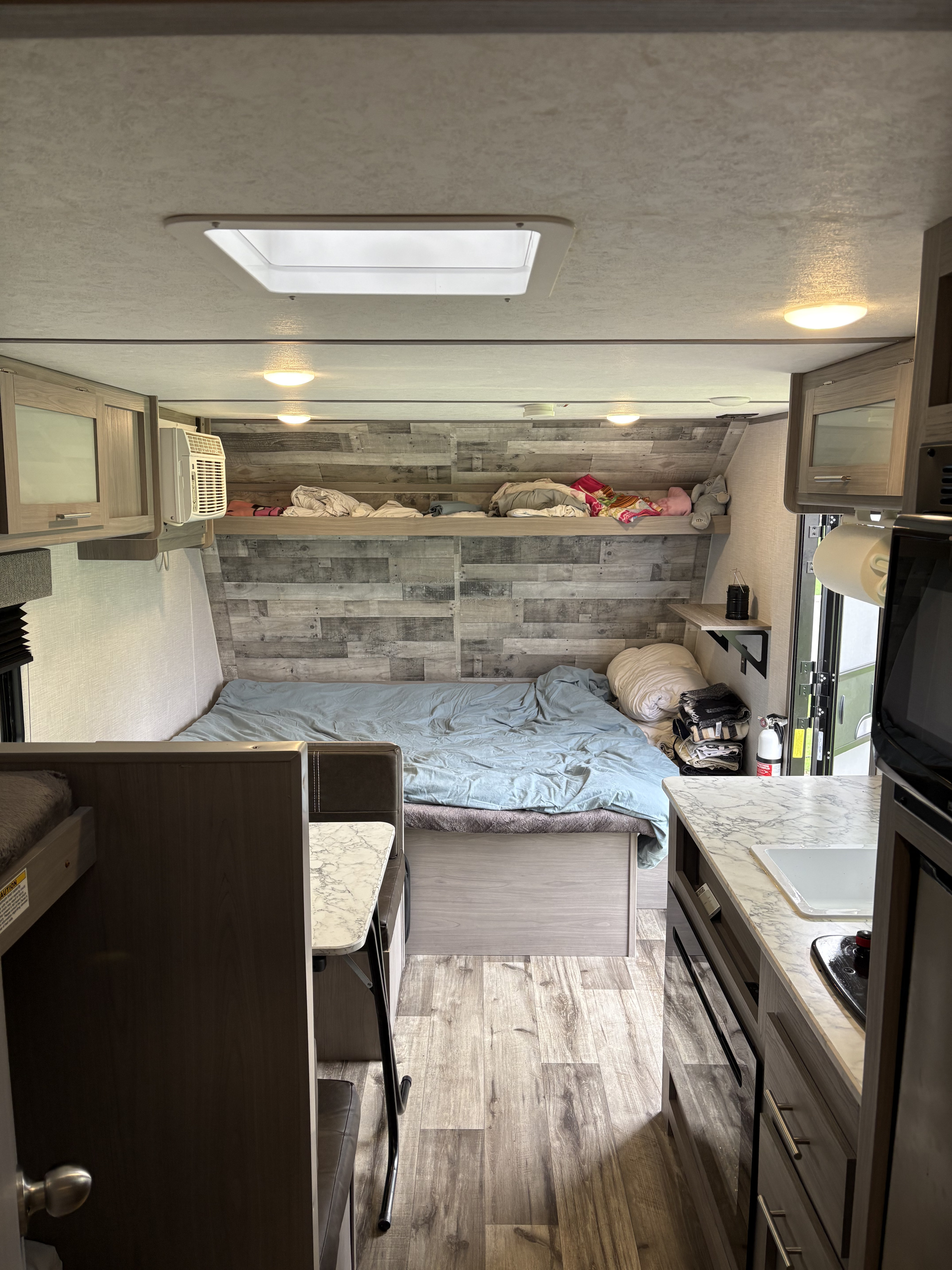 Compact rv rental interior: bed with blue sheets, kitchen counter with sink/stove, overhead cabinets, and bunk area for travel.. Coleman 17B 2023