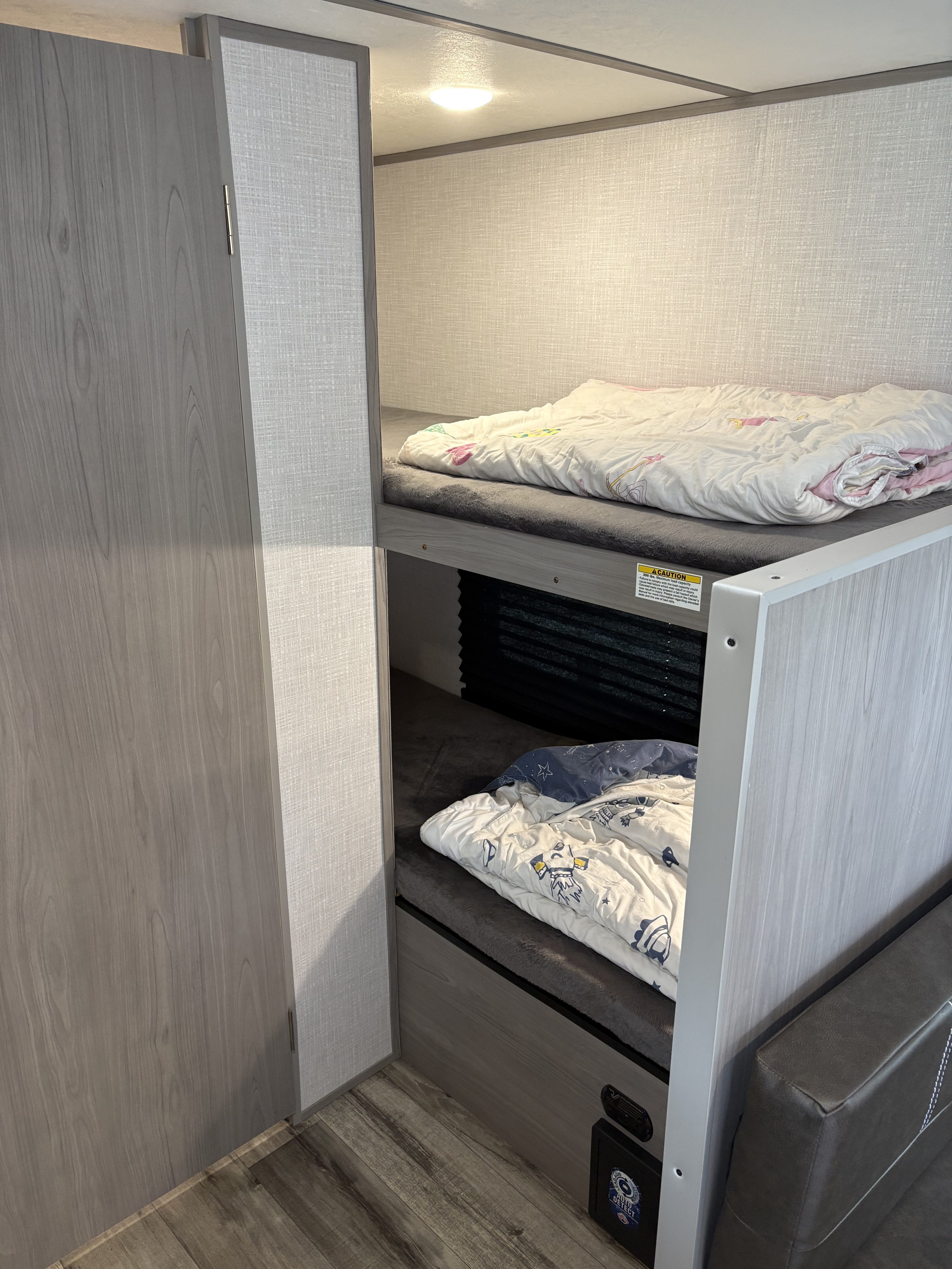 Comfortable RV rental bunk beds, upper and lower, with soft bedding, an overhead light, and a textured interior.. Coleman 17B 2023