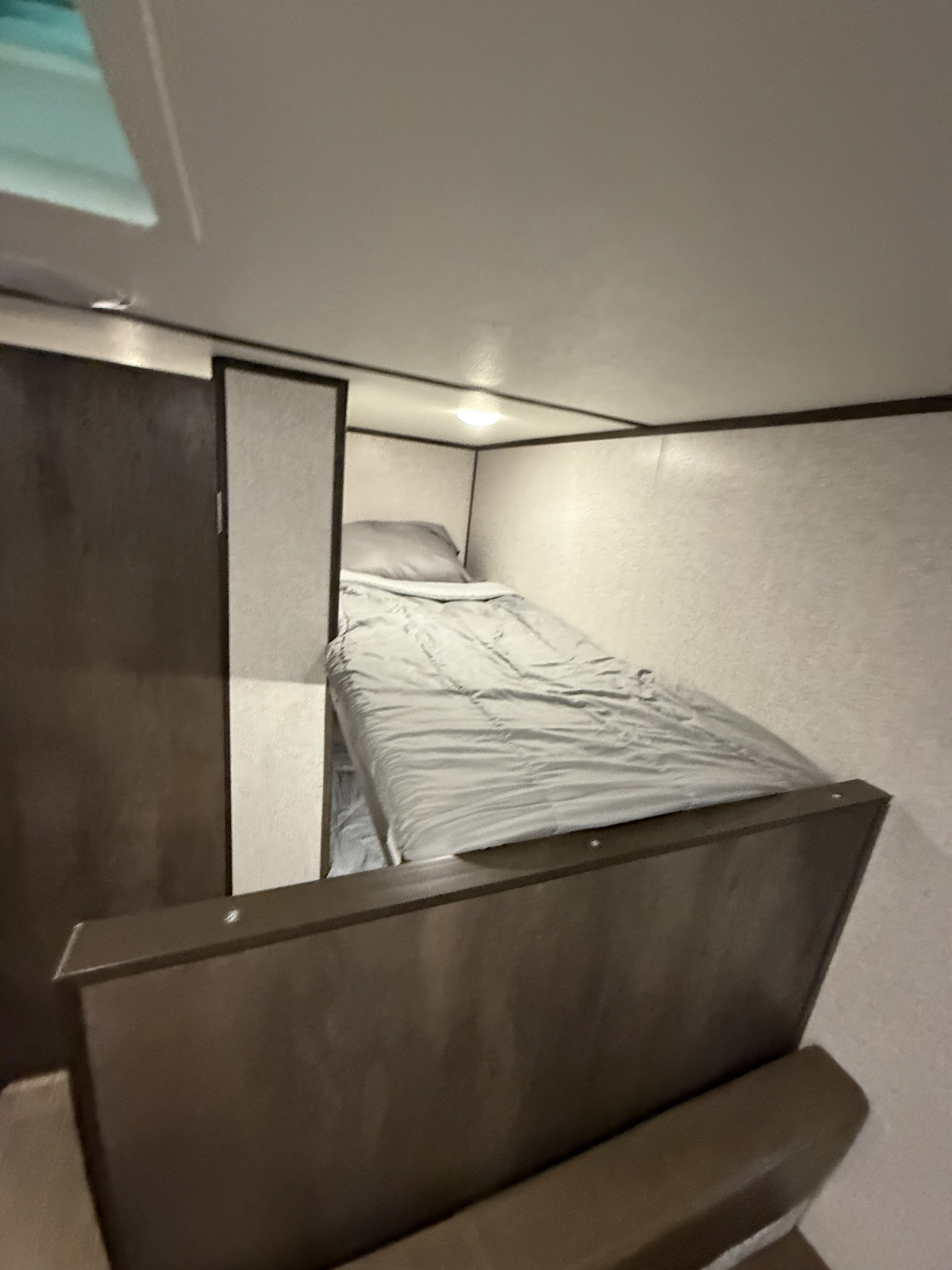 Inside an RV rental, a cozy bunk bed with gray bedding and a ceiling light. Dark brown paneling defines the compact sleeping area.. Dutchmen Coleman Lantern LT 2020
