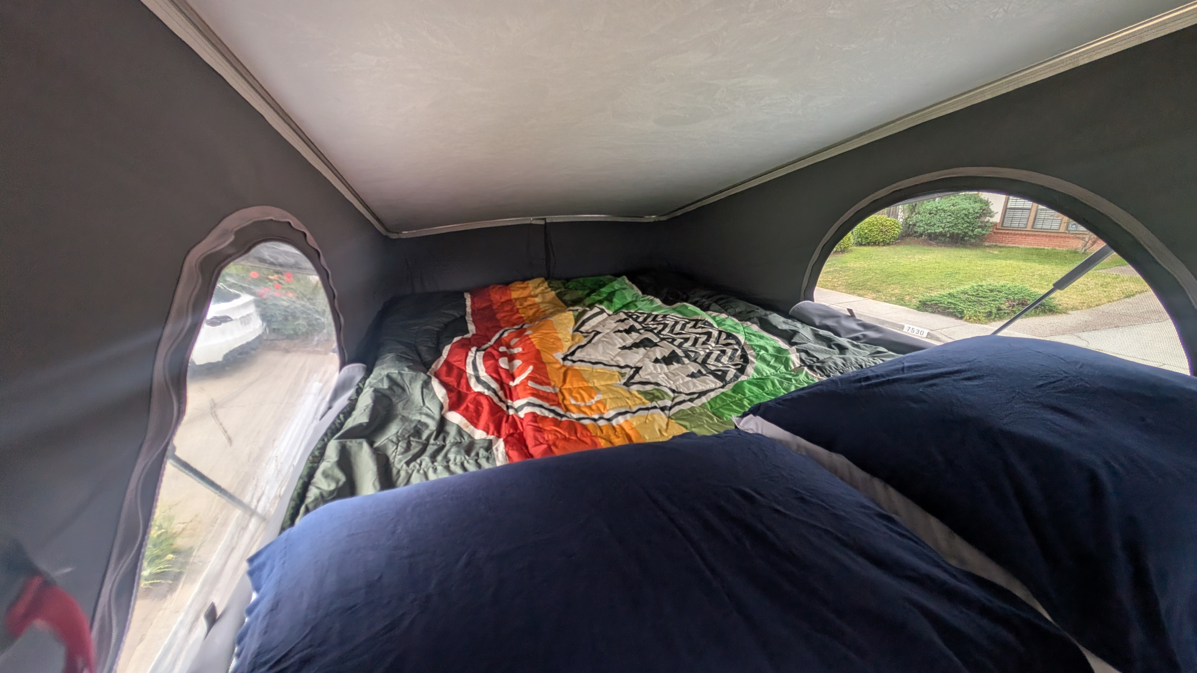 Cozy interior of an RV rental: a bed with colorful bedding & dark pillows, offering a view of a residential street through windows.. Winnebago Solis 2021