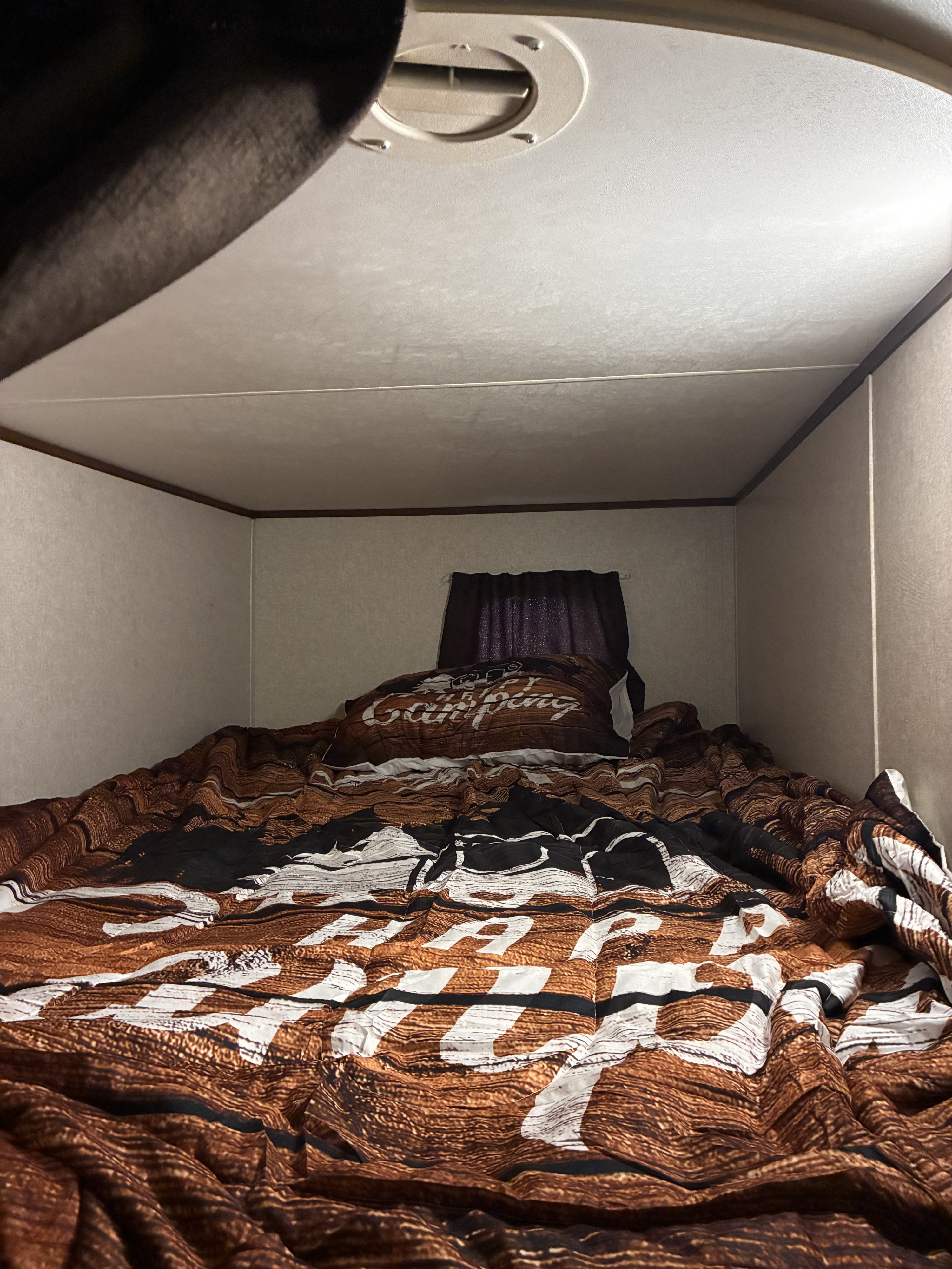 Inside a compact RV rental sleeping area: a bed with "Happy Camping" bedding, dark curtains, and an overhead vent.. Jayco Jay Flight SLX 2017