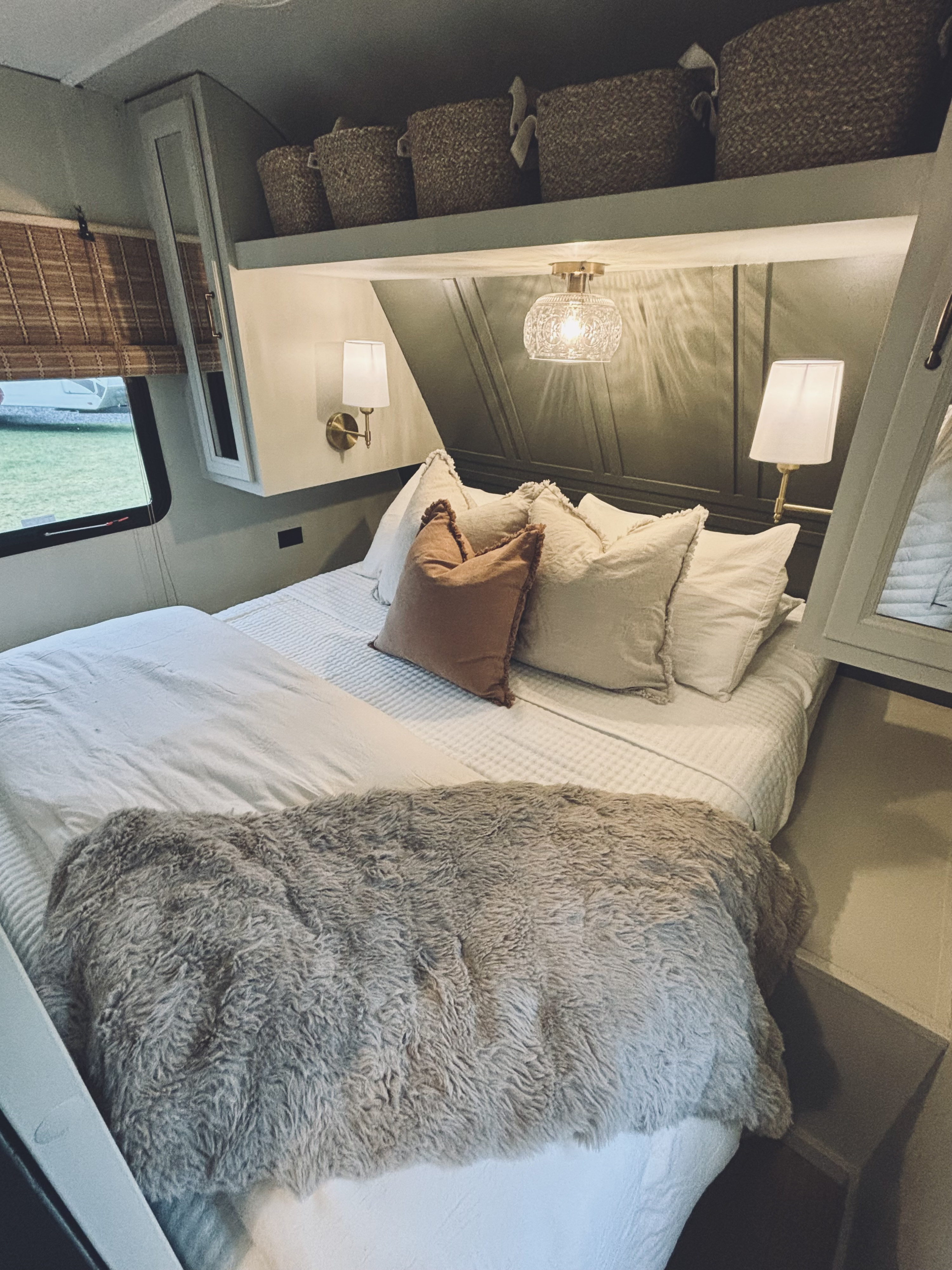 Cozy RV rental bedroom with white bedding, fluffy blanket, wall sconces, storage baskets, and a window view.. Highland Ridge RV Open Range 2022