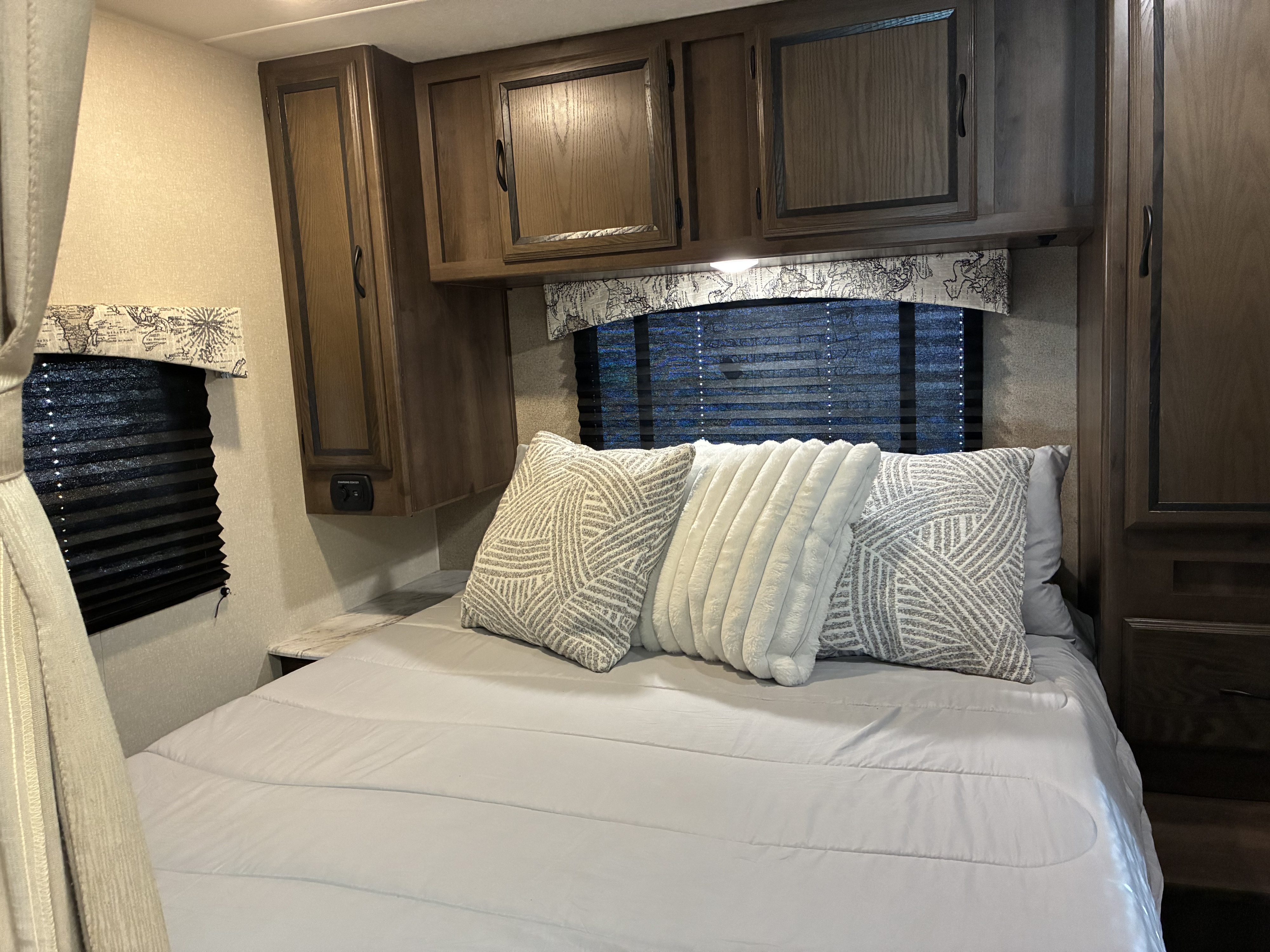 This inviting RV rental bedroom features a comfy bed with decorative pillows, overhead cabinets, and a window for a relaxing stay.. 1HA6GUCG3HN005063 27QBF 2018