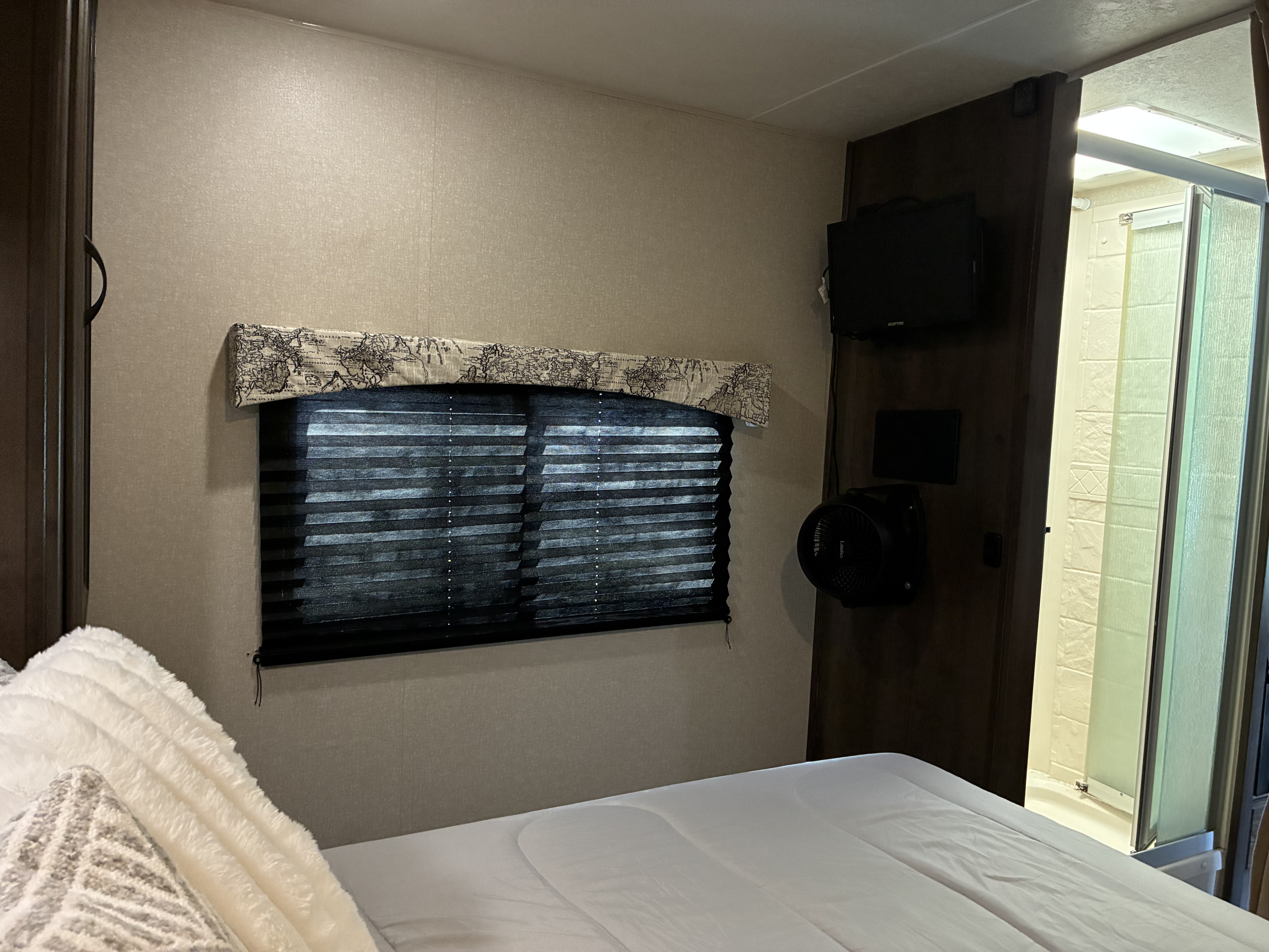 This RV rental bedroom features a comfortable bed, window with closed blinds, TV, fan, and an adjacent shower.. 1HA6GUCG3HN005063 27QBF 2018