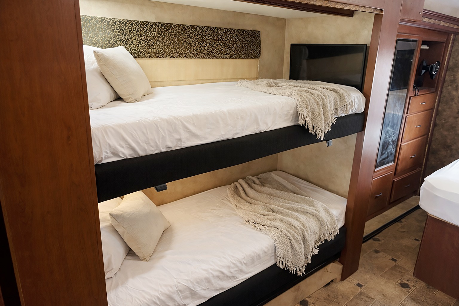 RV rental interior featuring comfortable bunk beds with white linens, throws, a TV, and wooden storage.. Thor Hurricane 2014