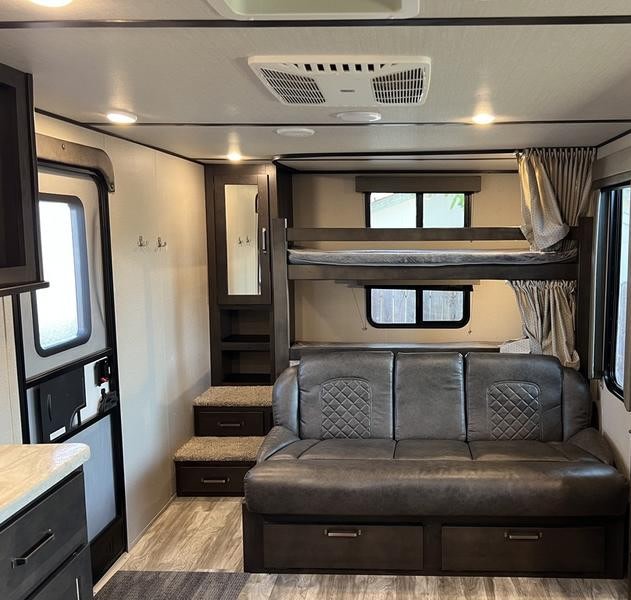 RV rental living area featuring a dark leather sofa, bunk beds, and entryway with storage.. Grand Design Transcend Xplor 2021