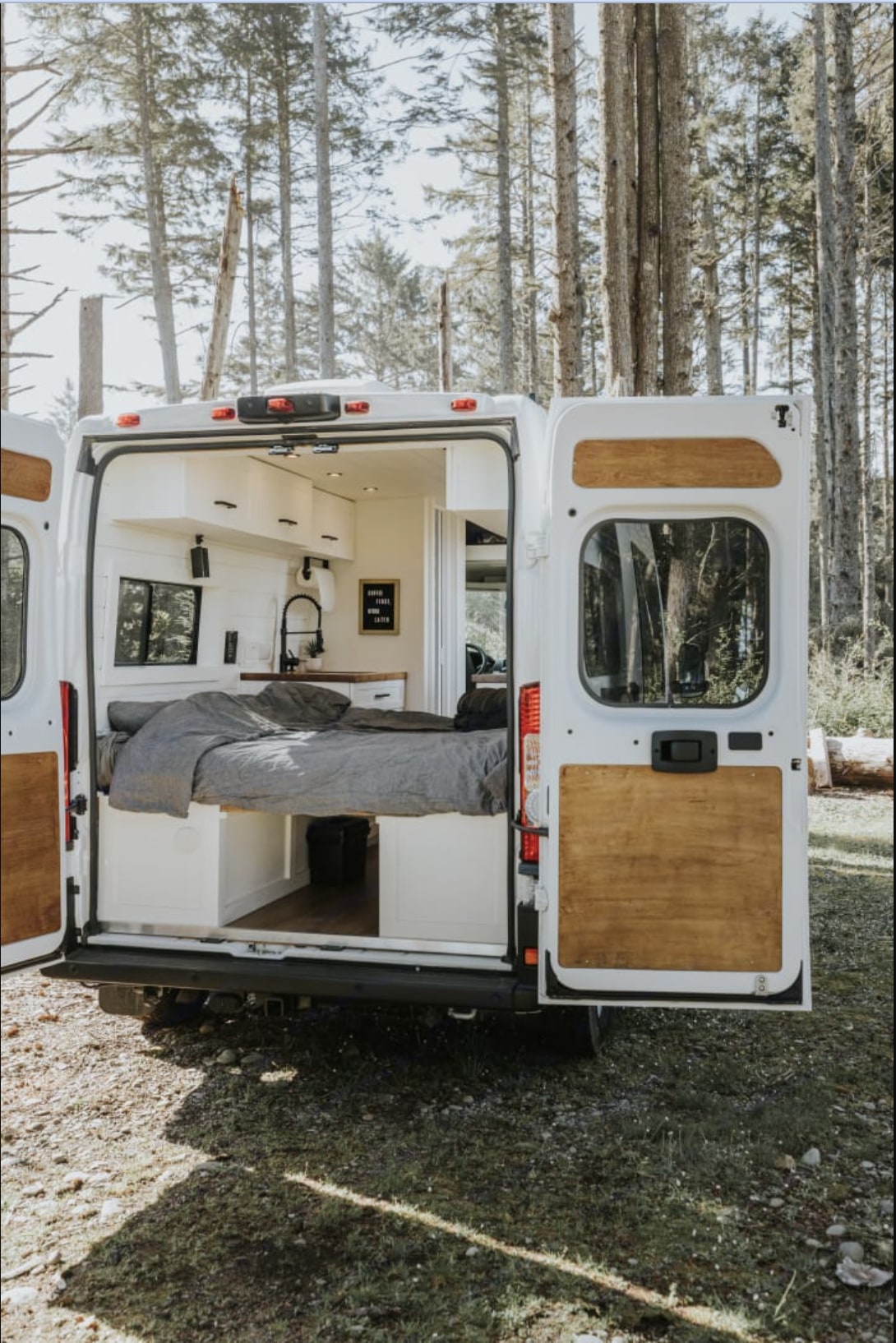 Explore nature! This modern rv rental camper van features open back doors revealing a cozy bed, kitchen, and cabinets.. Ram ProMaster 2023