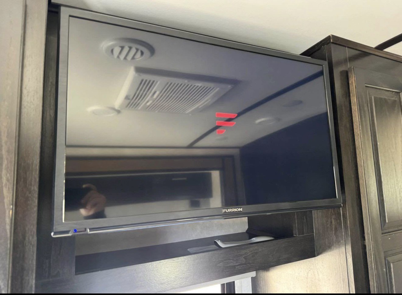 Mounted Furrion TV inside an rv rental, reflecting ceiling vents and lights. Dark wood cabinets frame the screen.. FR3 FR3 Motorhome 2019