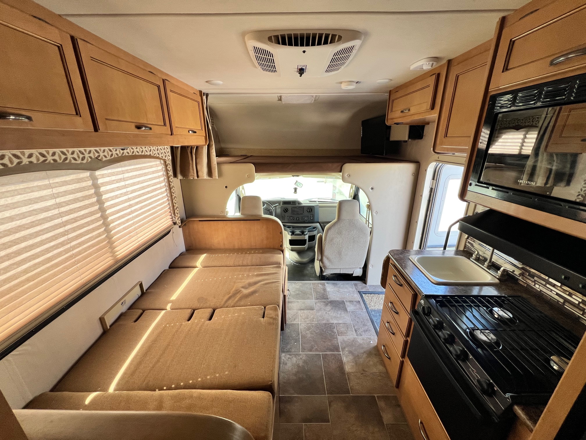 Spacious rv rental interior with full kitchen (stove, sink, microwave), comfortable sofa bed, overhead cabinets, and front cockpit.. Thor Four Winds 2016